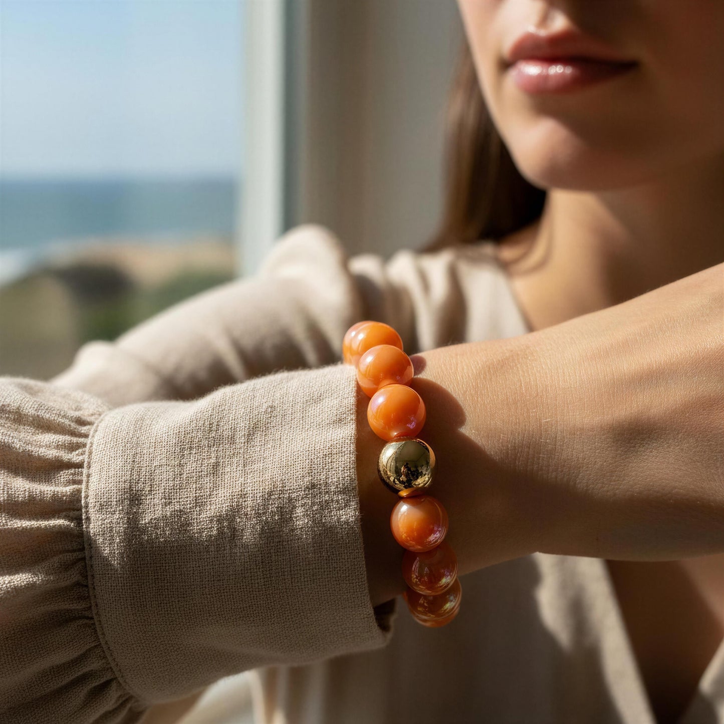 Model wearing a bracelet with orange beads and a gold accent, with a blurred outdoor background.