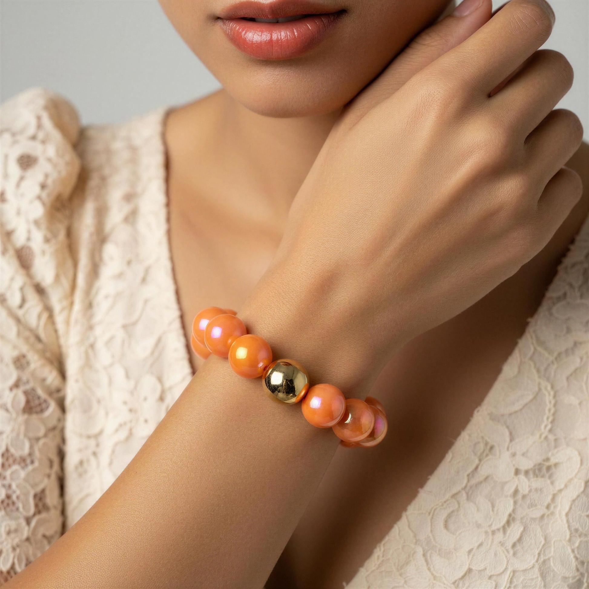 Close-up of a wrist wearing an orange beaded bracelet with a gold bead on a neutral background.
