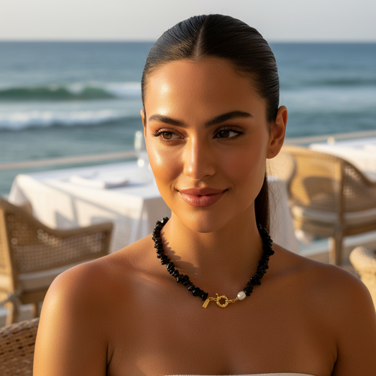 Woman wearing a black beaded necklace with a key pendant by the ocean.