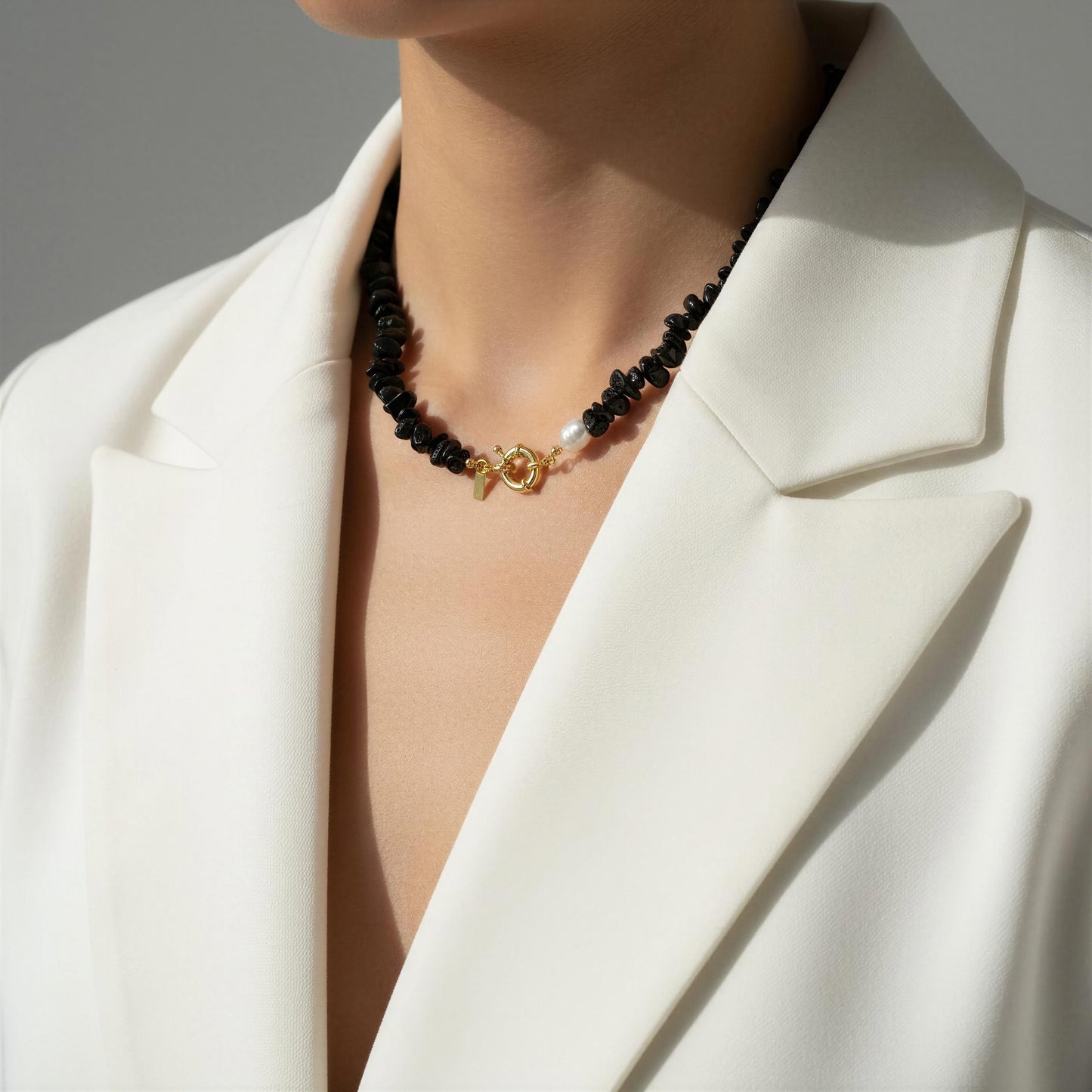 The Midnight Tide Necklace with black beads and a gold clasp worn by a person in a white blazer.