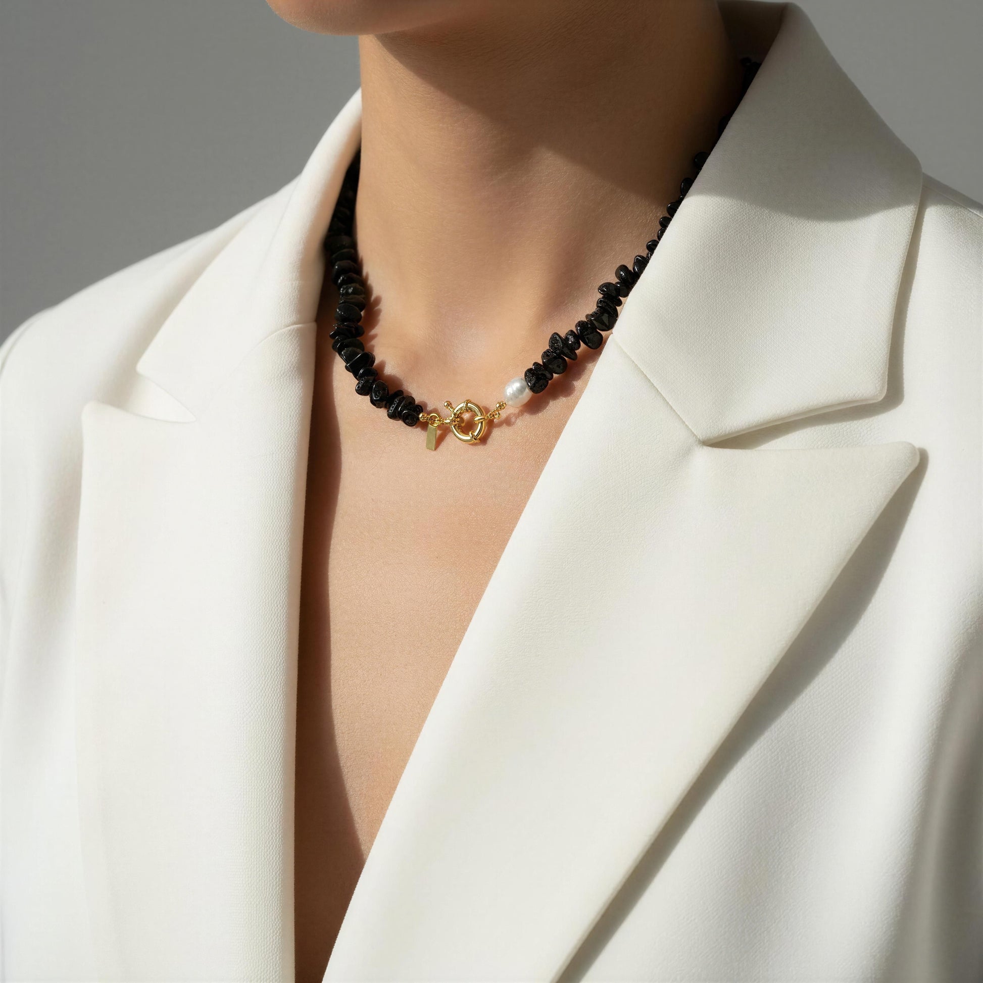 The Midnight Tide Necklace with black beads and a gold clasp worn by a person in a white blazer.