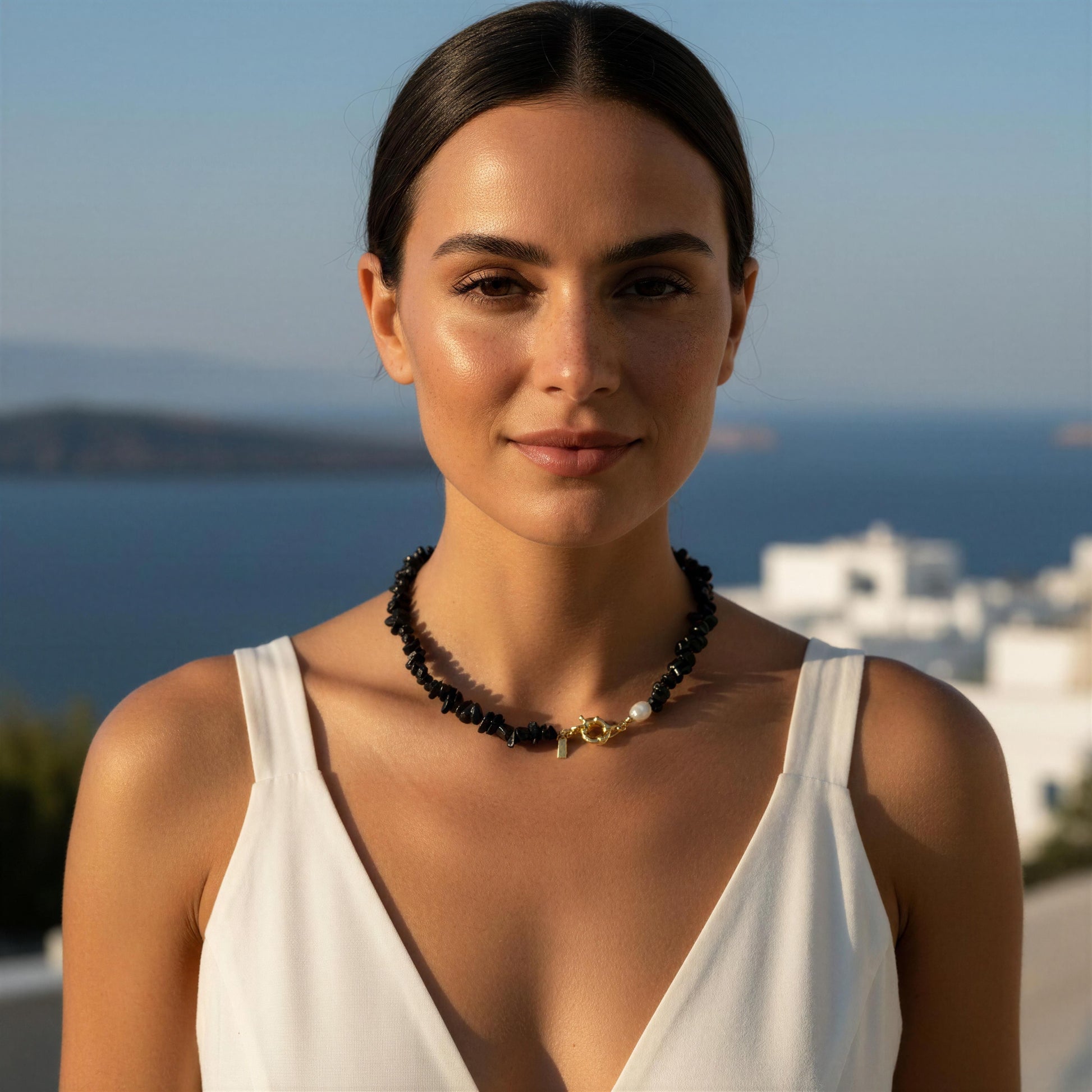 Woman wearing a white dress with a scenic background of the ocean and buildings wearing the Midnight Tide Necklace