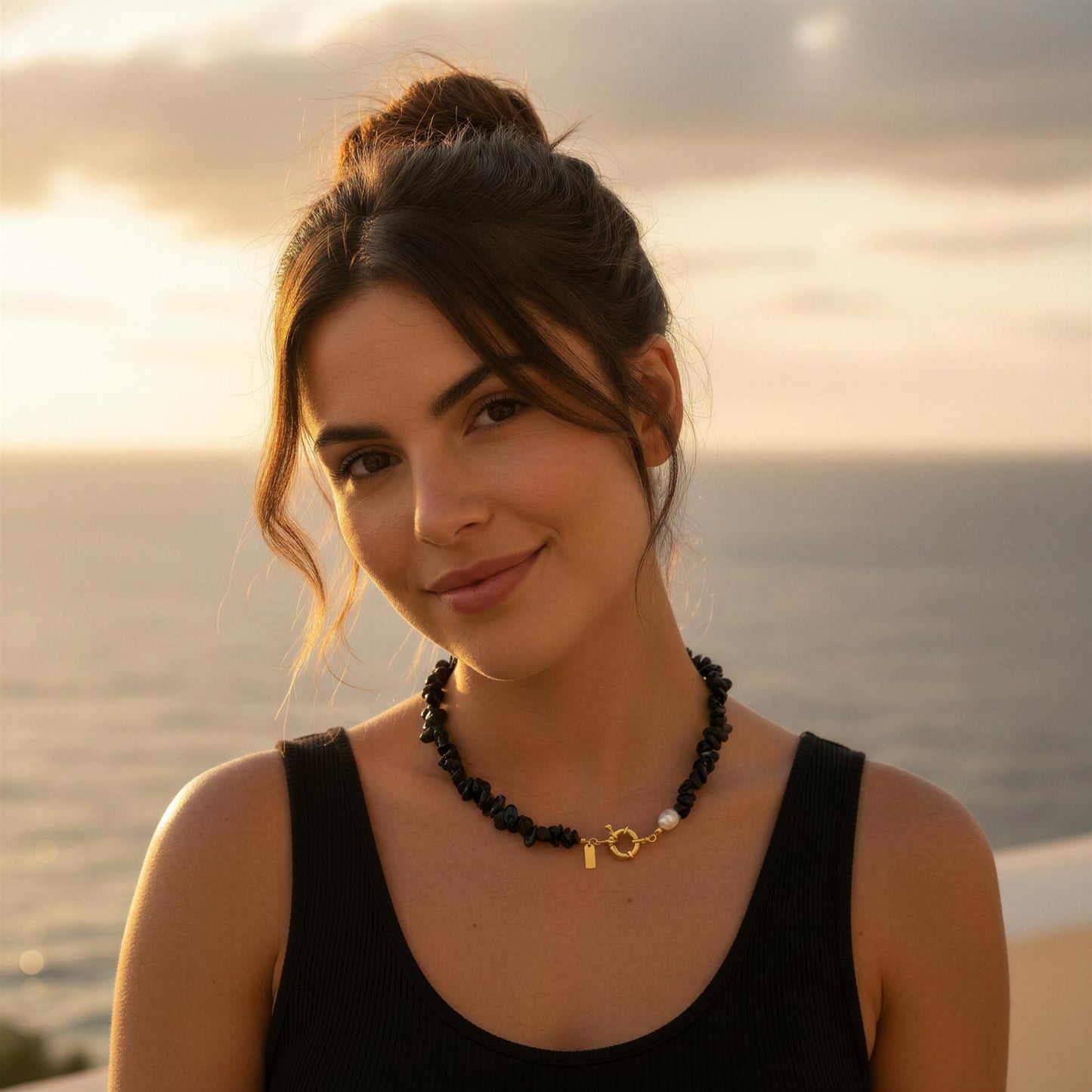 Woman wearing a black tank top and the Midnight Tide Necklace with a sunset or sunrise background