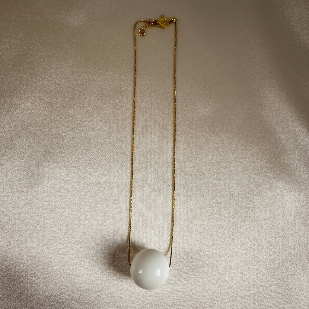 The Milky Bead Necklace with a white spherical pendant on a beige fabric background