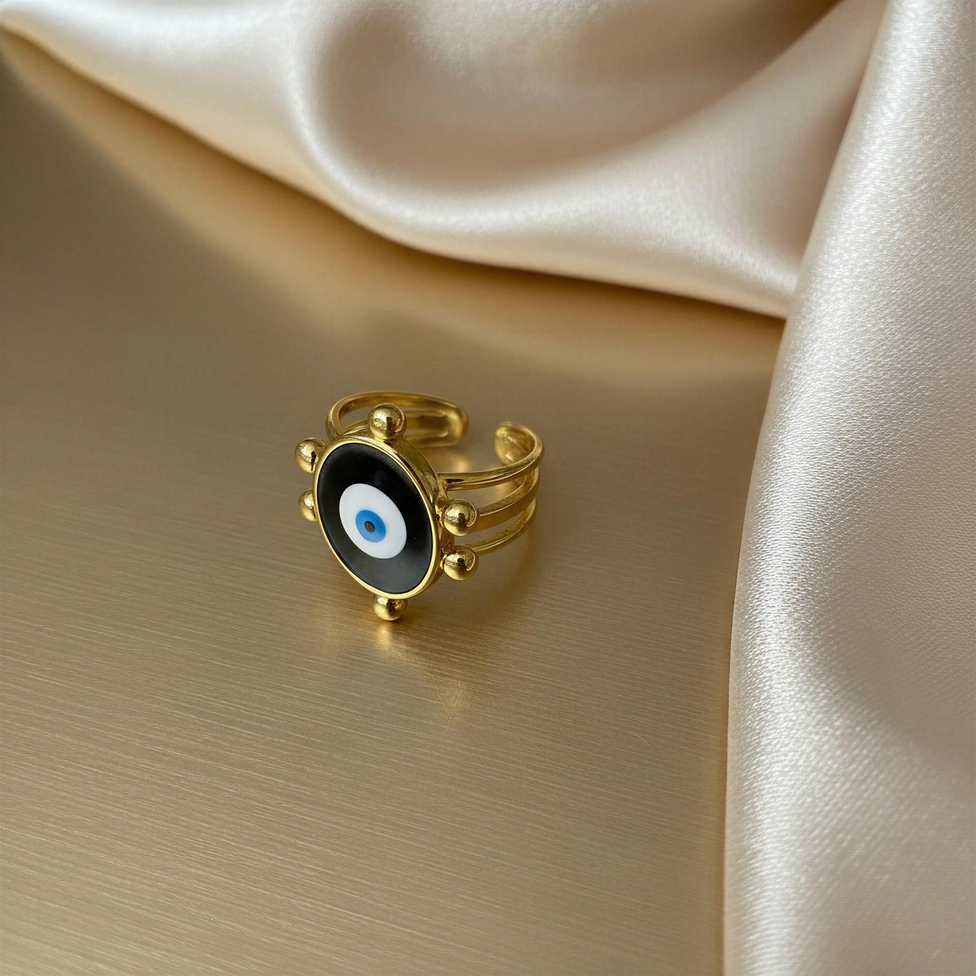 Gold ring with a black and blue eye design on a beige fabric background