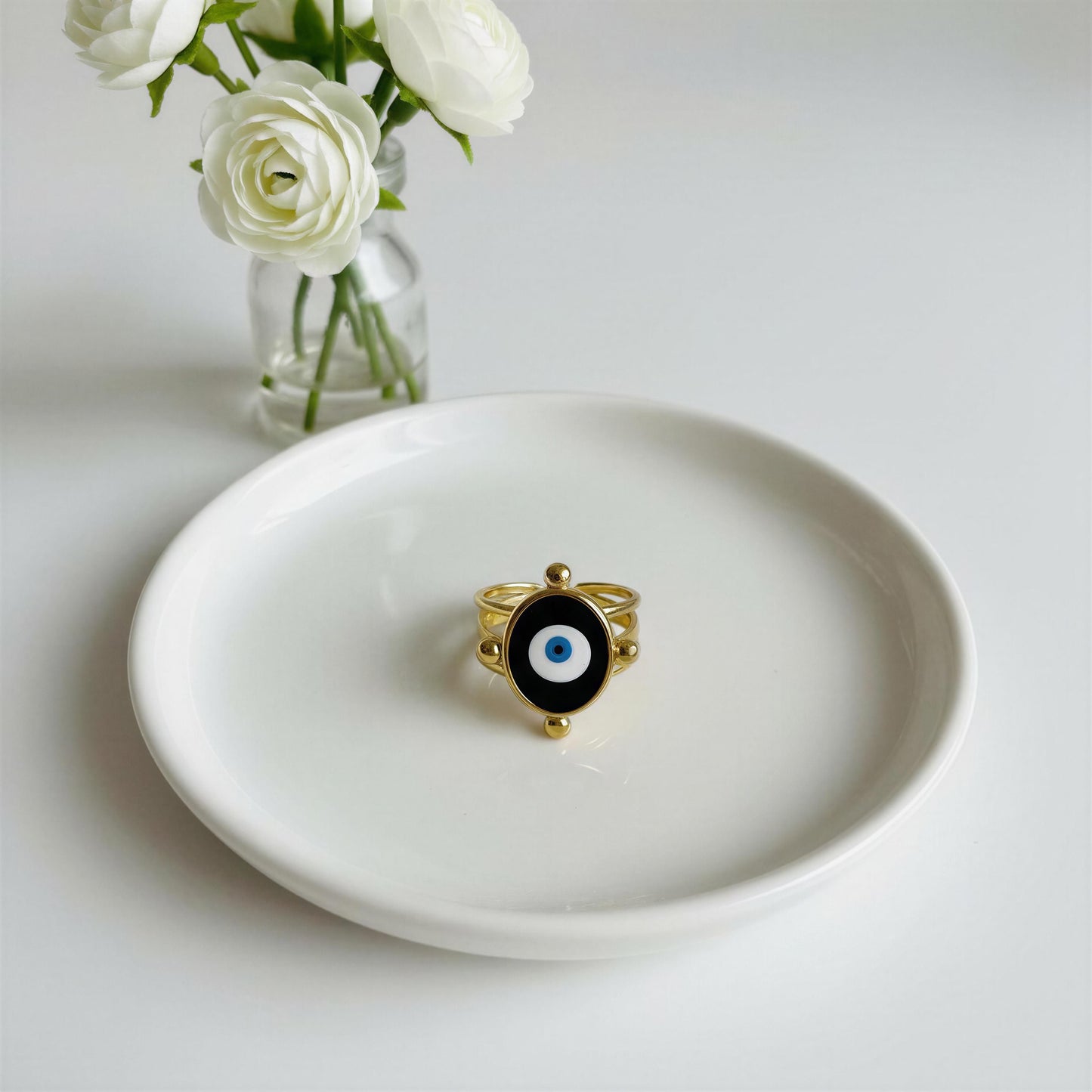 The Nazar Aura Ring Gold on a white plate with white flowers in the background