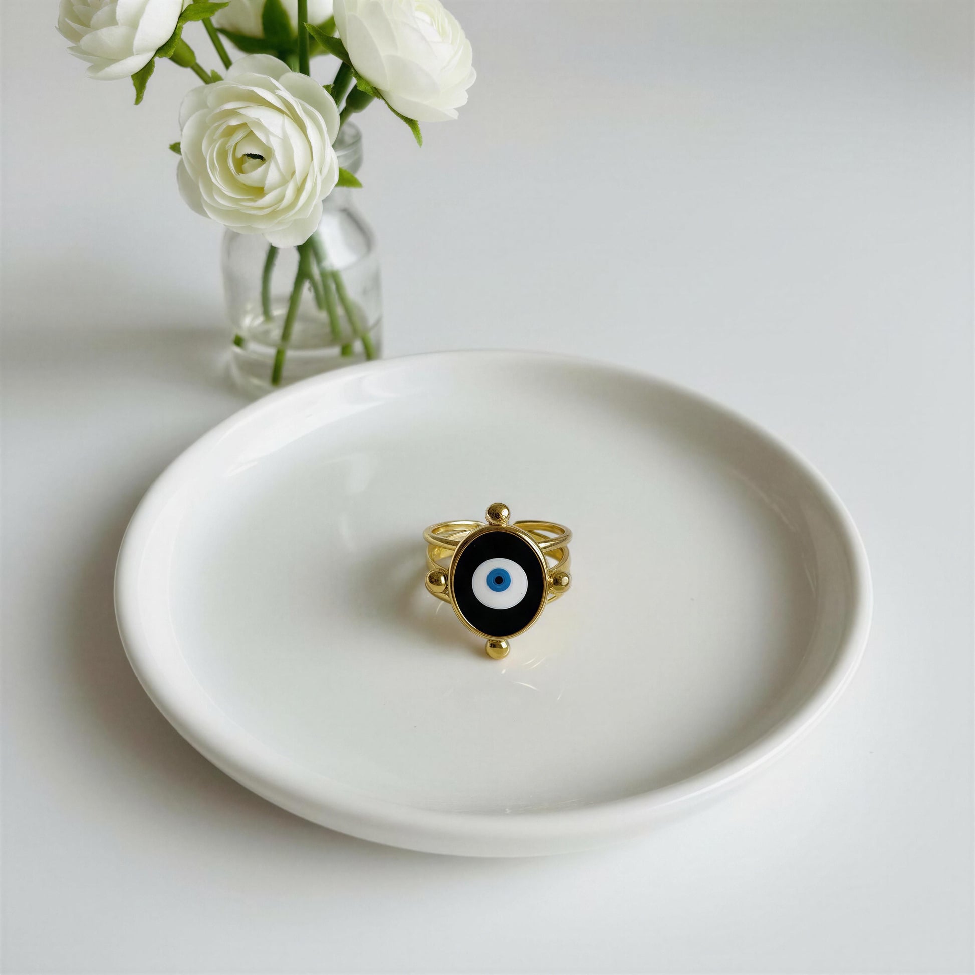 The Nazar Aura Ring Gold on a white plate with white flowers in the background