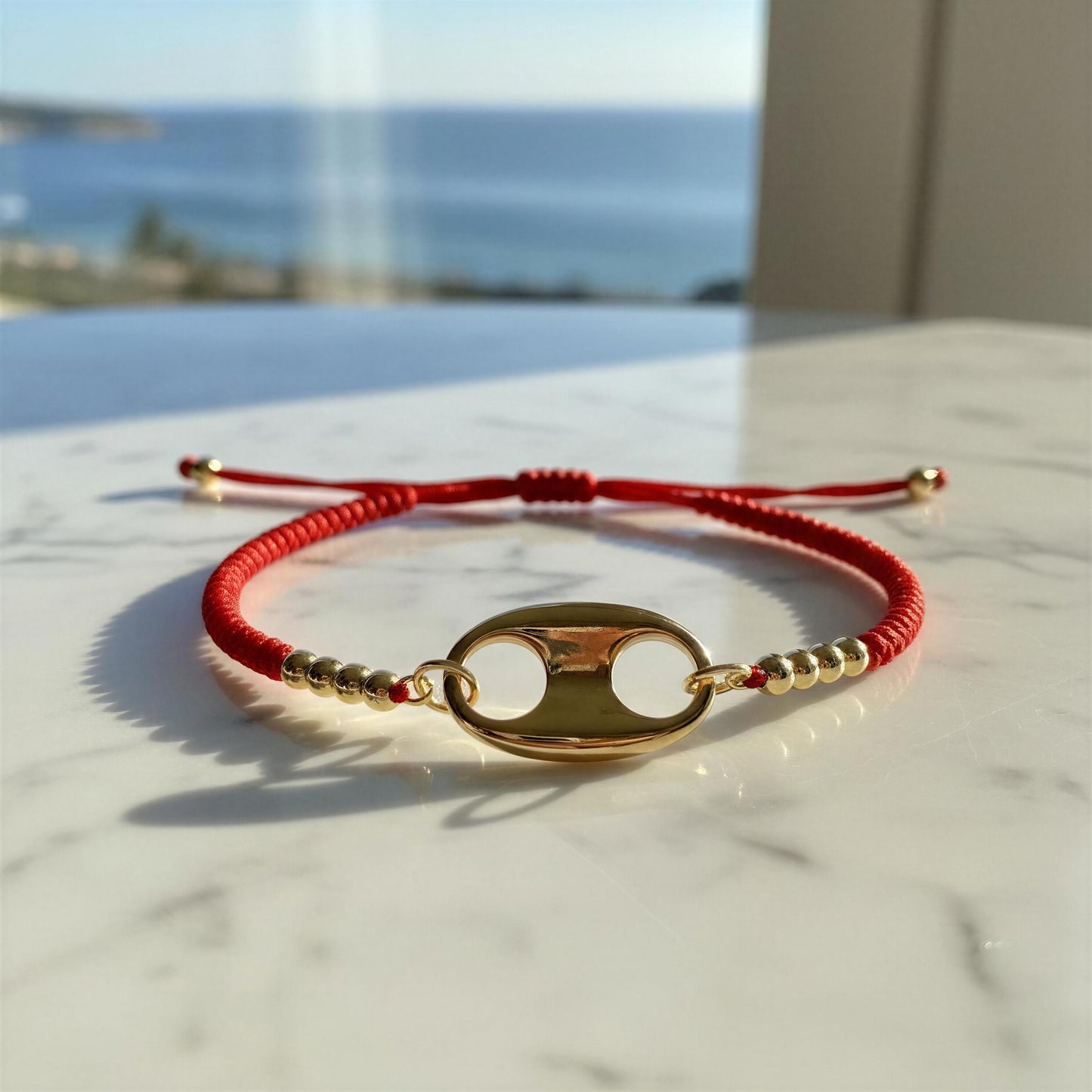 Red bracelet with gold charm on a marble surface with ocean view