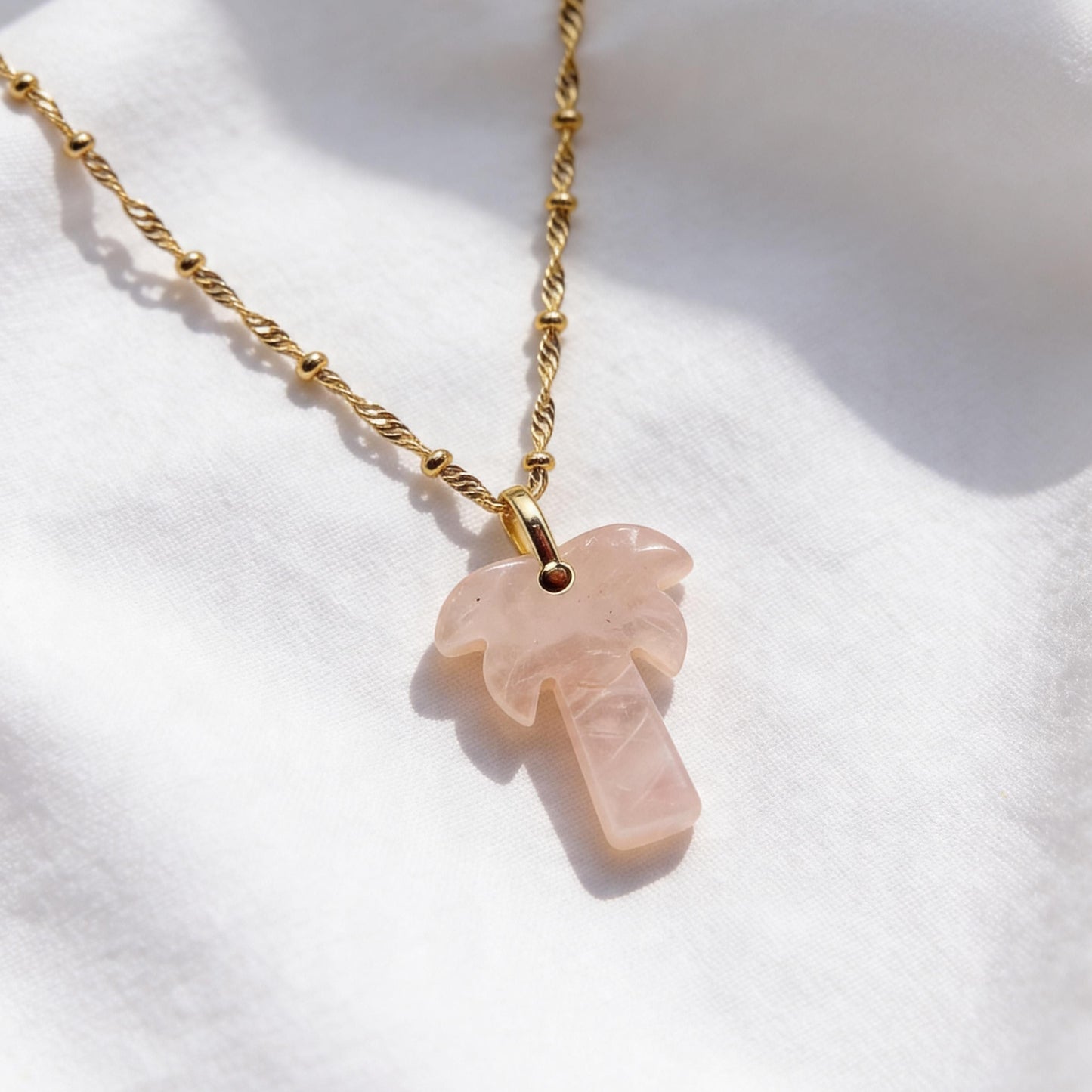 The Palma Rosa Long Necklace on a white fabric background