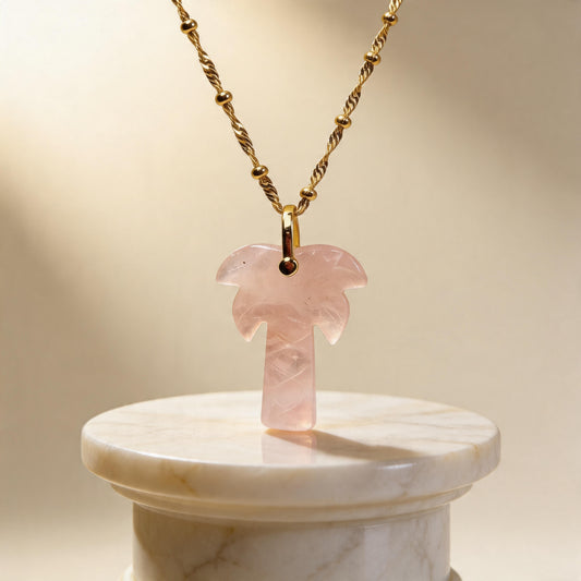 Pink palm tree pendant necklace on a marble stand with a beige background