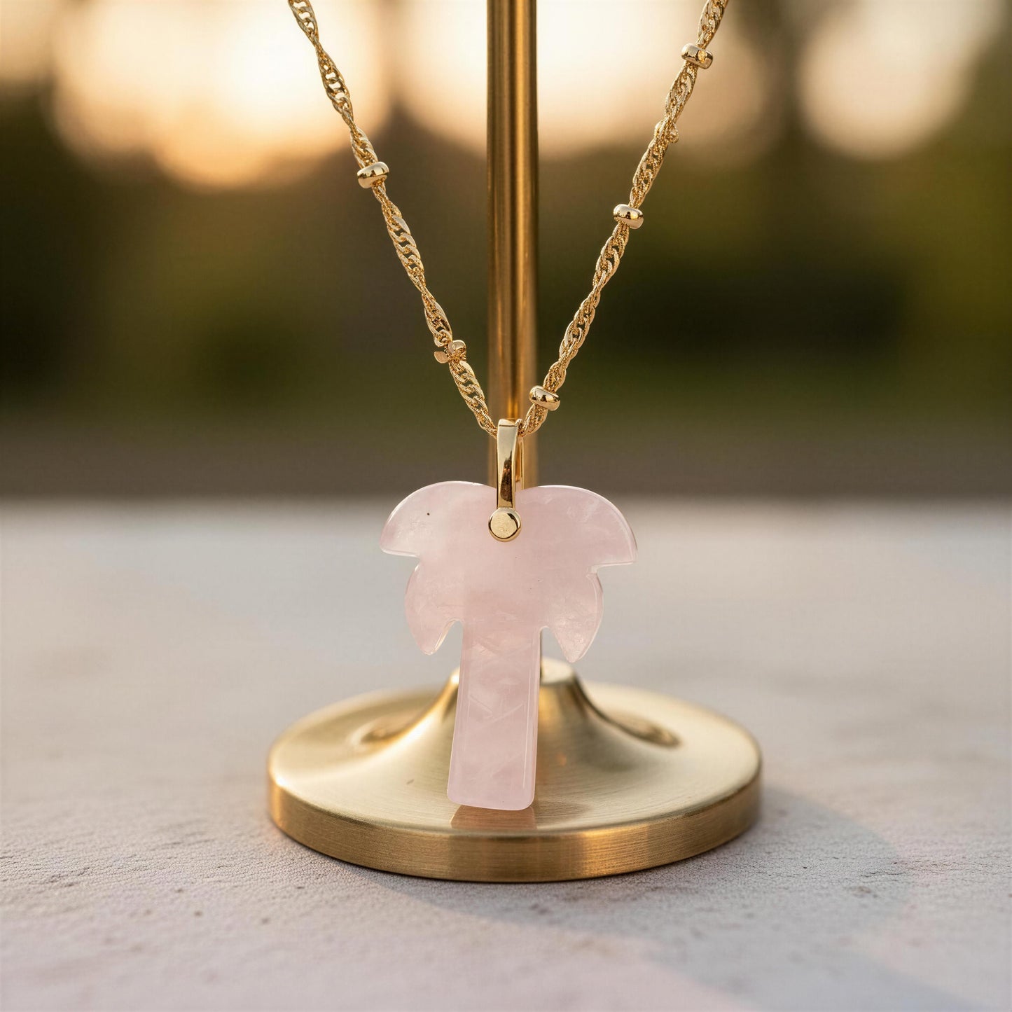 Necklace with a pink palm tree pendant on a gold stand against a blurred natural background