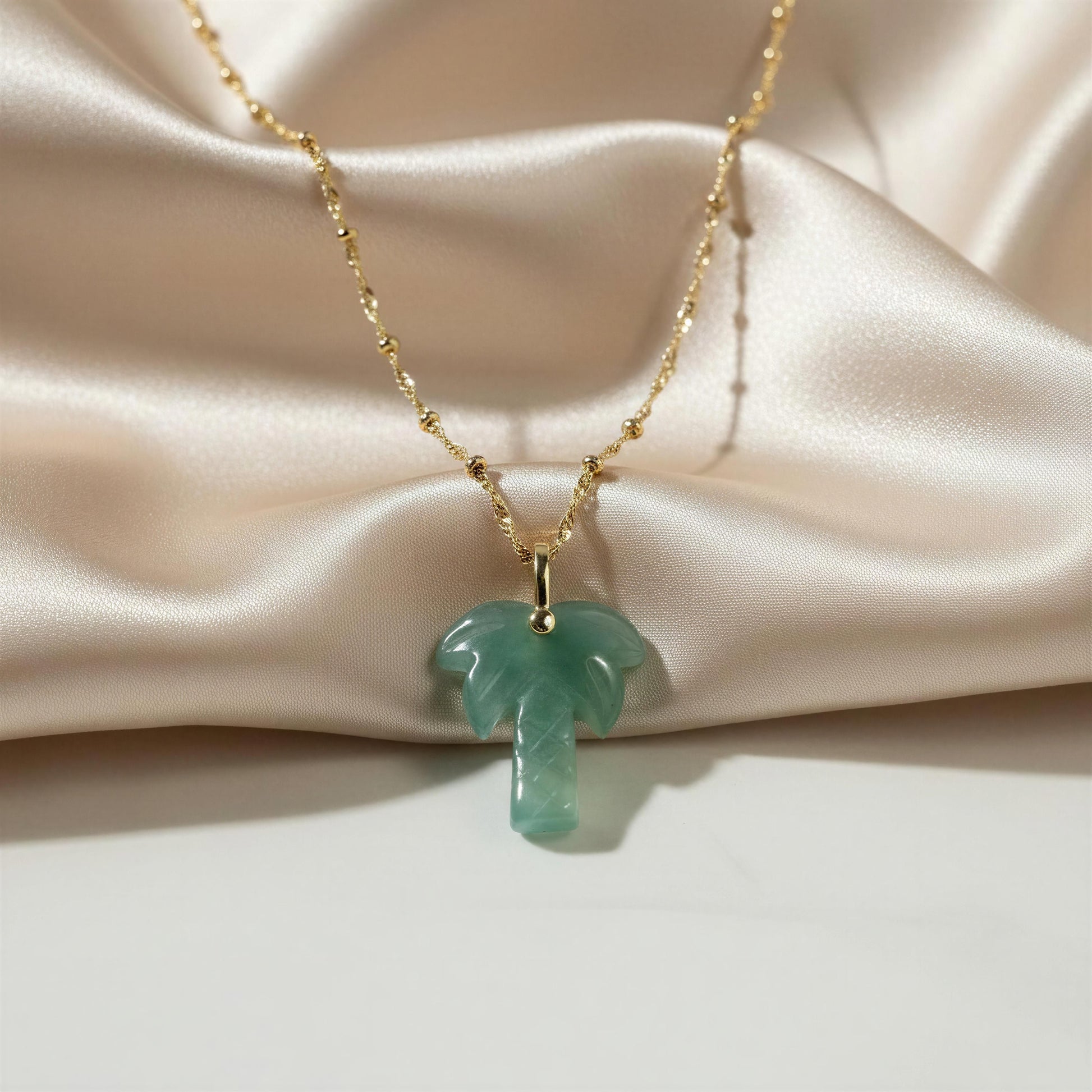 Necklace with a green palm tree pendant on a beige fabric background