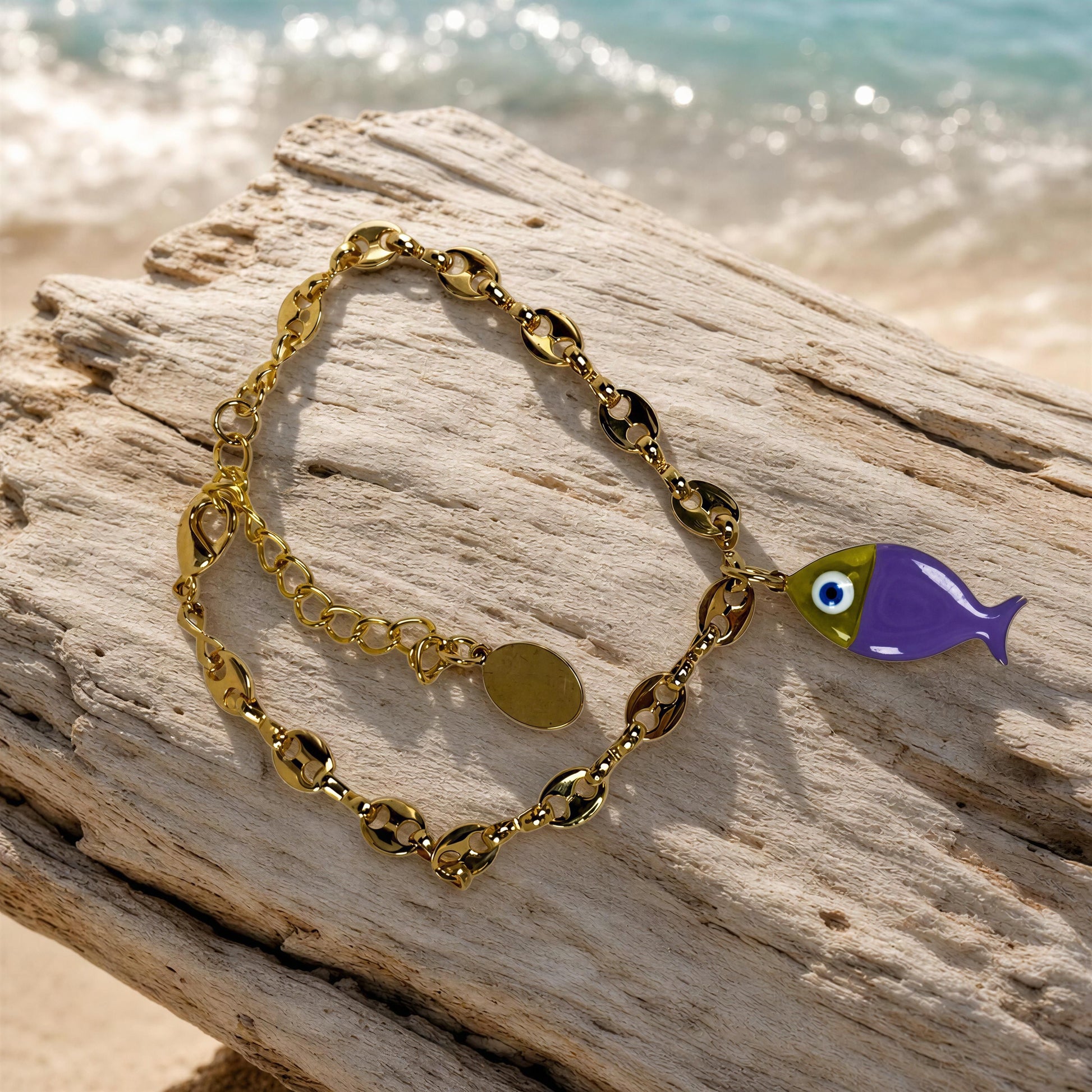 The Pesca Lila Bracelet with a fish charm on a piece of driftwood by the beach