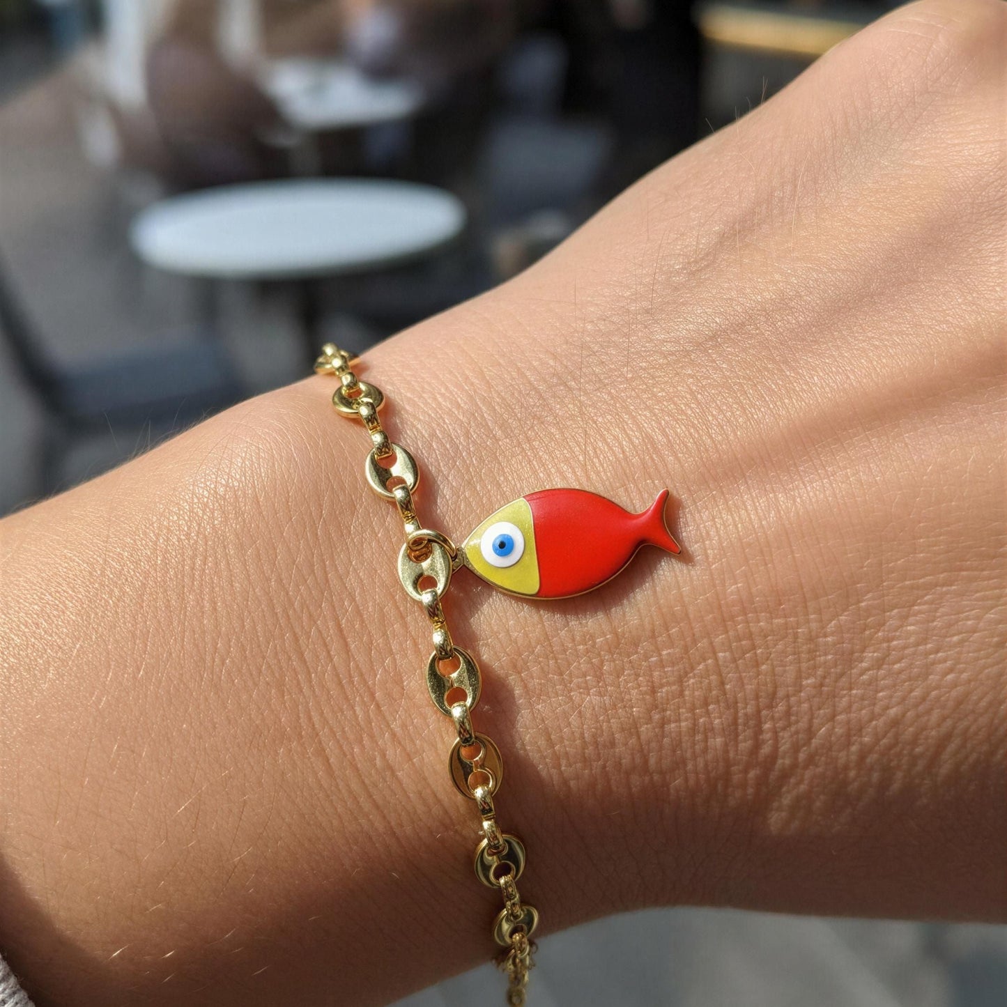 Gold bracelet with a red fish charm on a wrist, blurred restaurant background