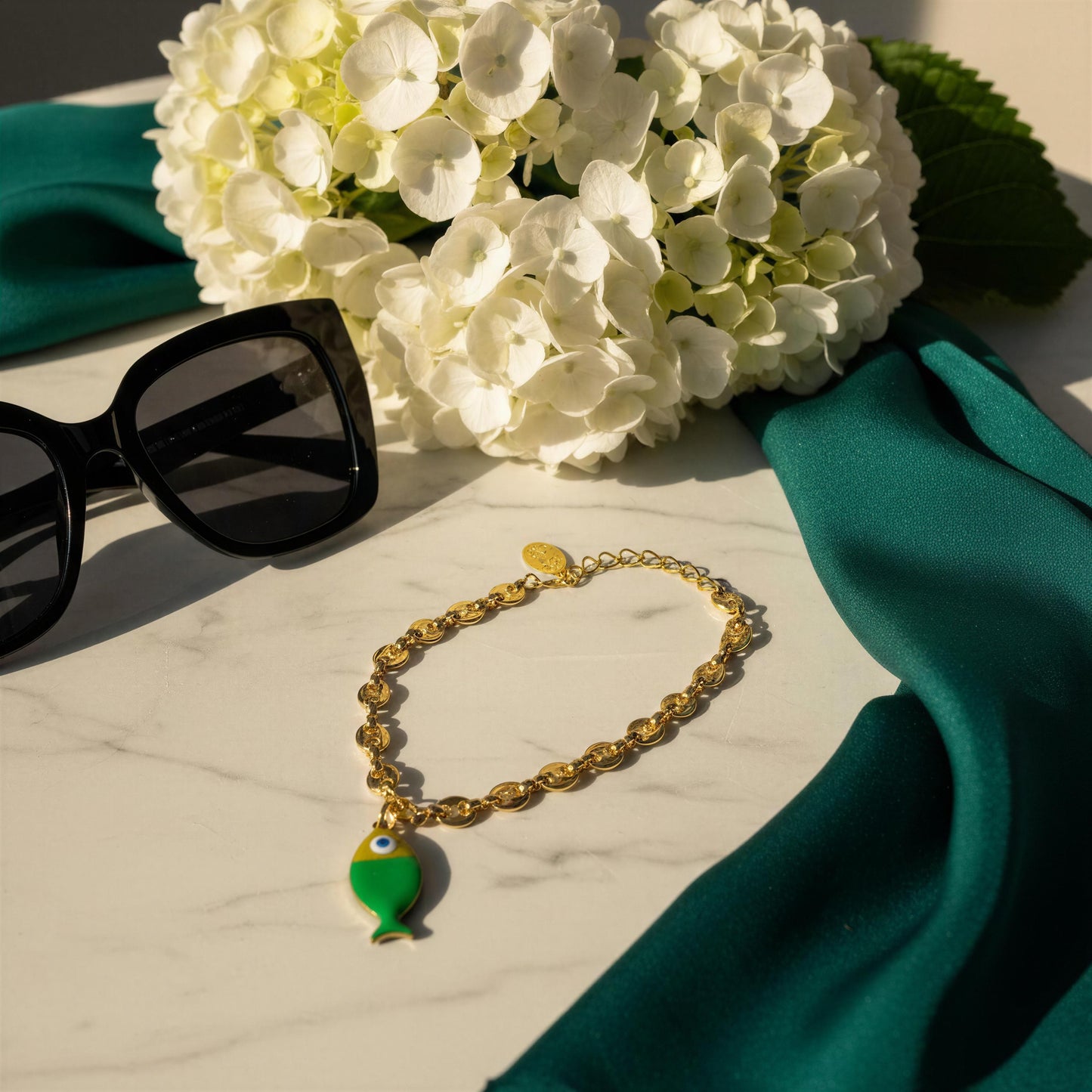 The Pesca Verde Bracelet on a marble surface with white flowers and sunglasses.