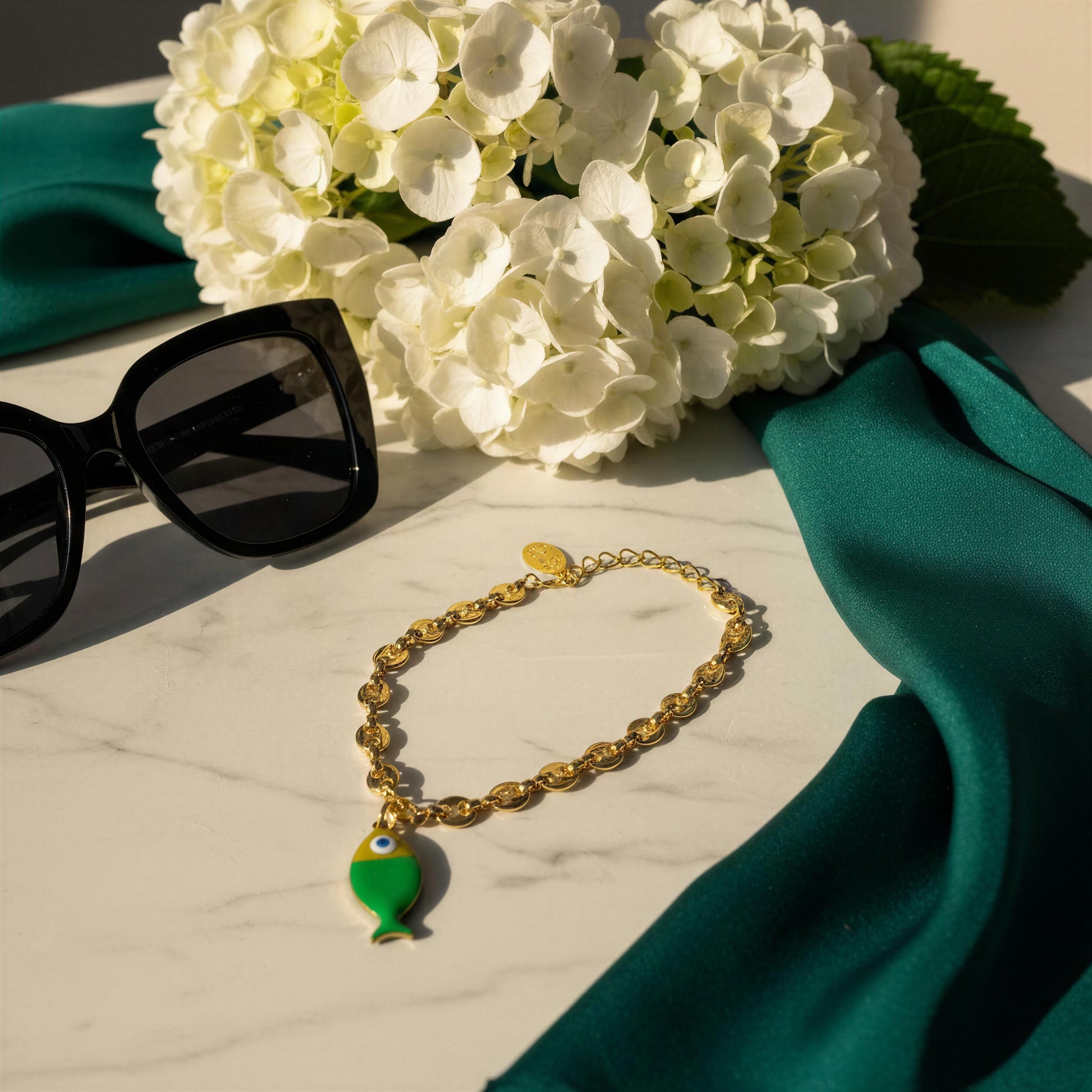 The Pesca Verde Bracelet on a marble surface with white flowers and sunglasses.