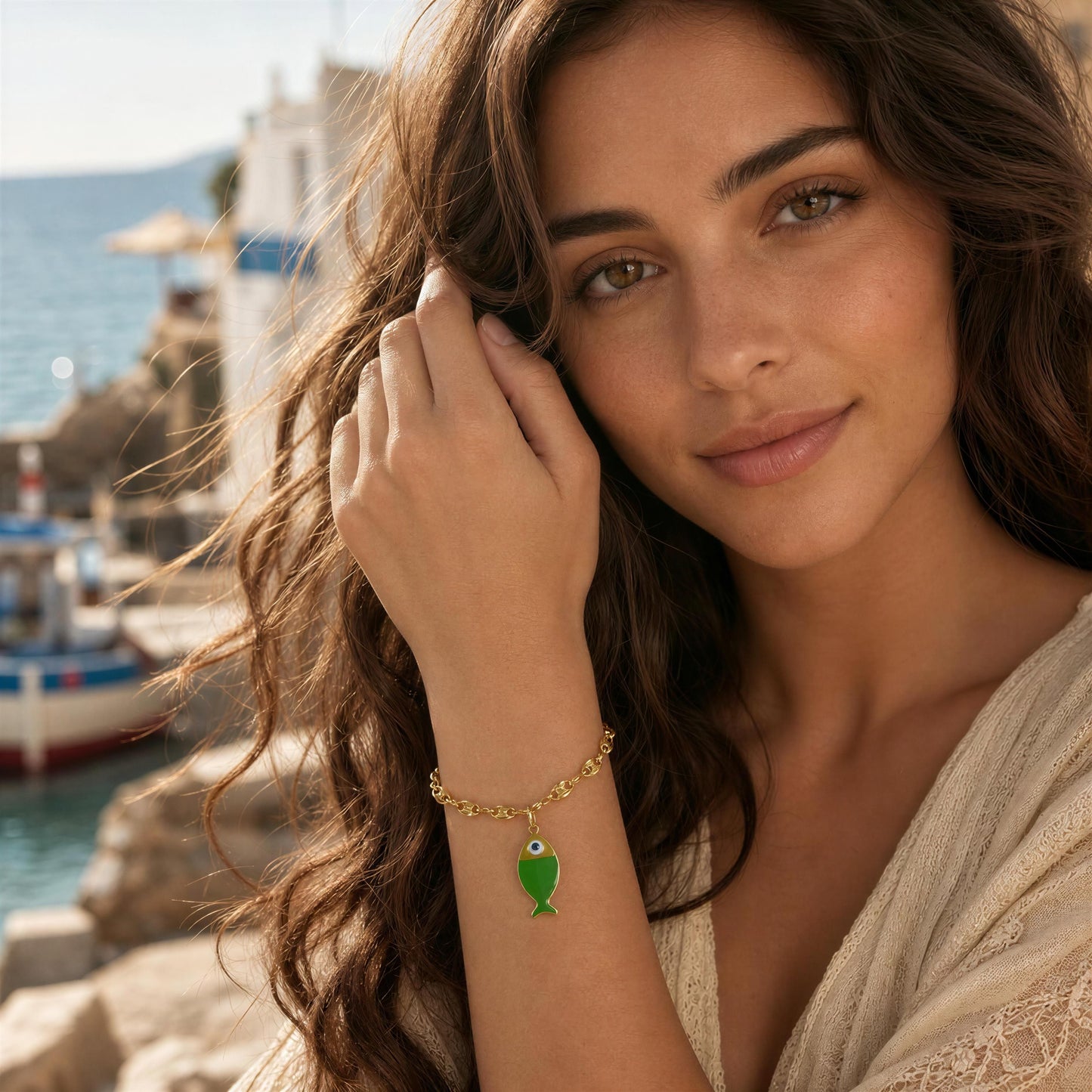 Woman wearing a gold bracelet with a green fish charm by a waterfront