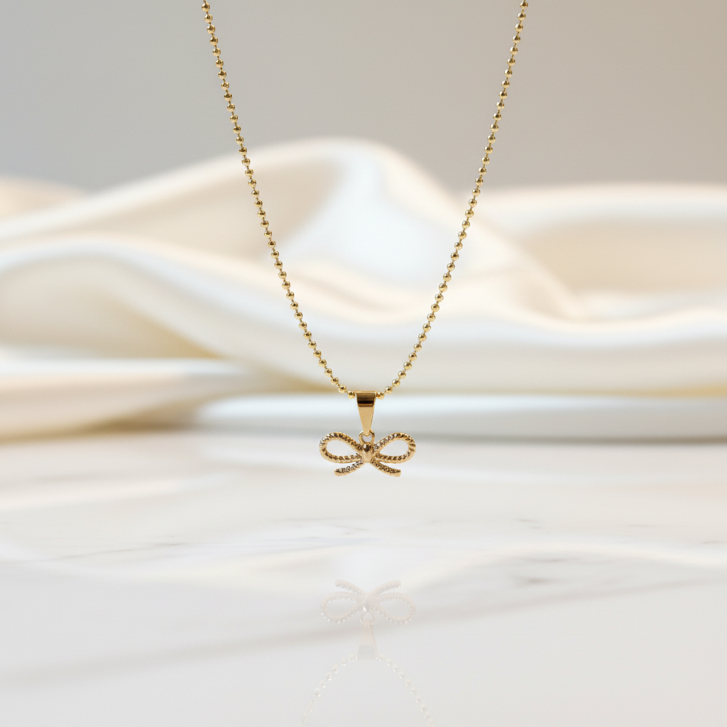 Gold Chica Chica Jewelry necklace with a bow pendant on a soft white fabric background
