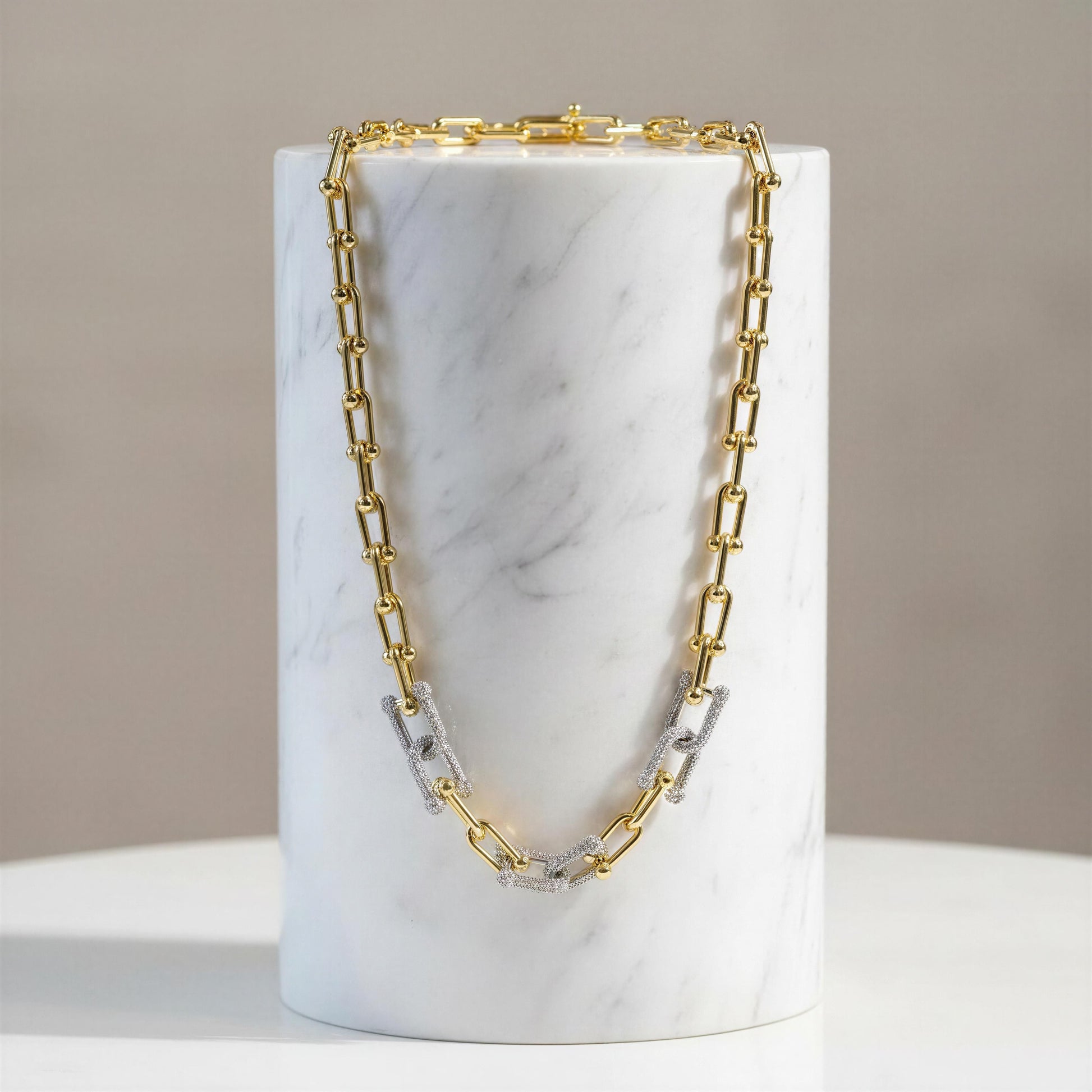 Gold and silver chain necklace on a marble stand with a neutral background