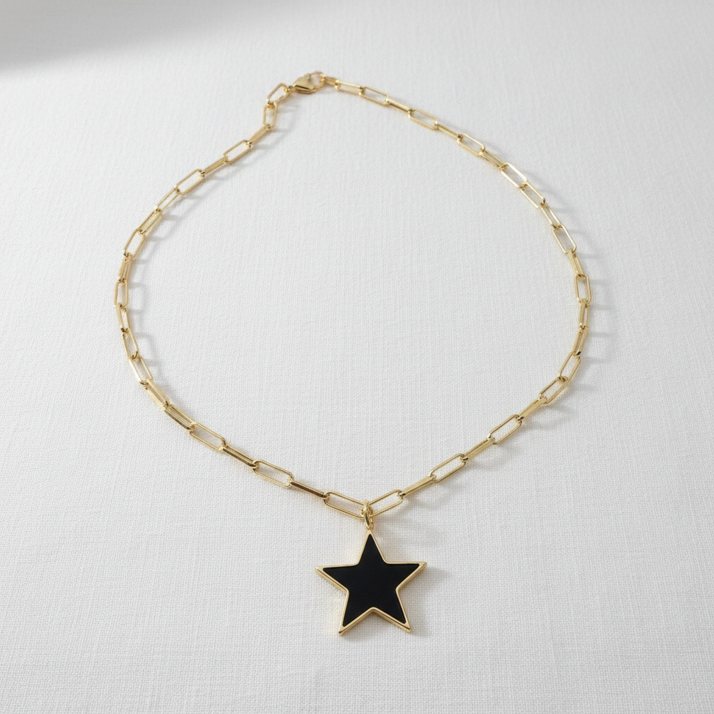 Gold chain paperclip necklace with a black star pendant on a white background. Radiant Noir Star Necklace from Chica Chica Jewelry 