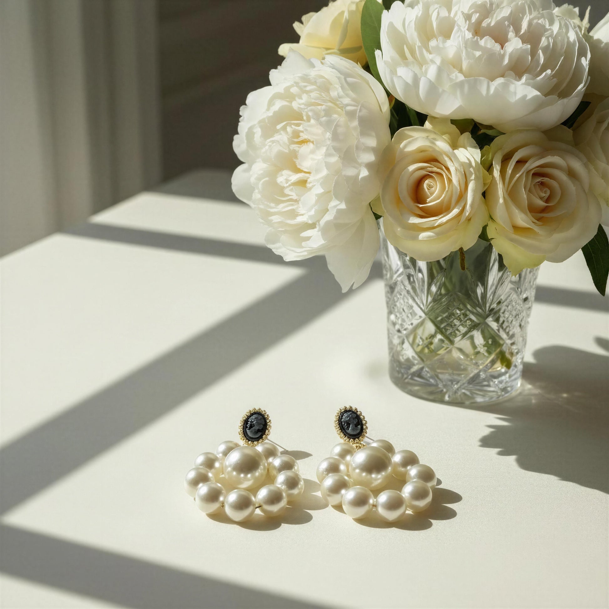 The Regal Cameo Pearl Statement Earrings on a table with a vase of white flowers.
