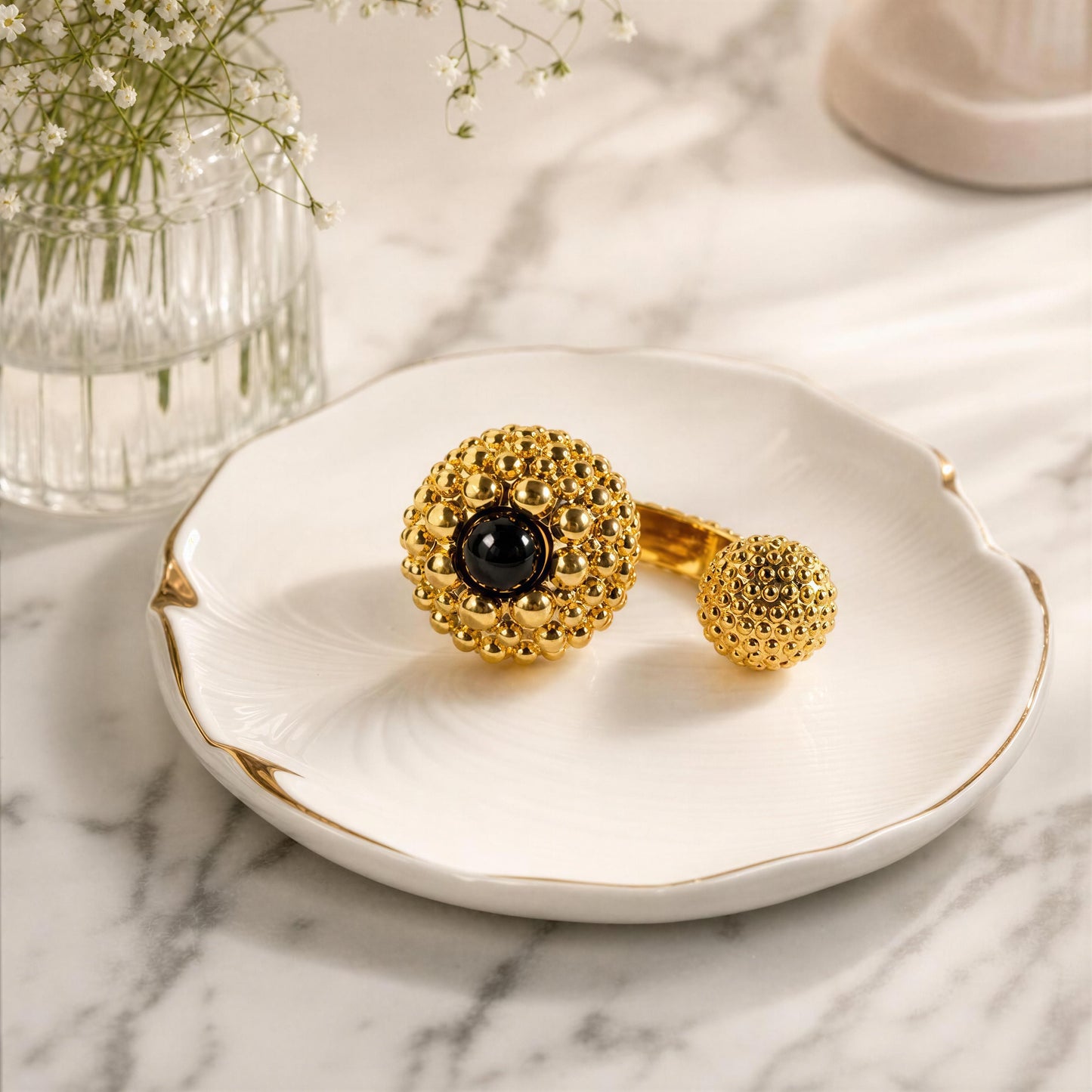 The Nero Ring from Chica Chica Jewelry, displayed on a white scalloped dish with gold trim over a marble surface.
