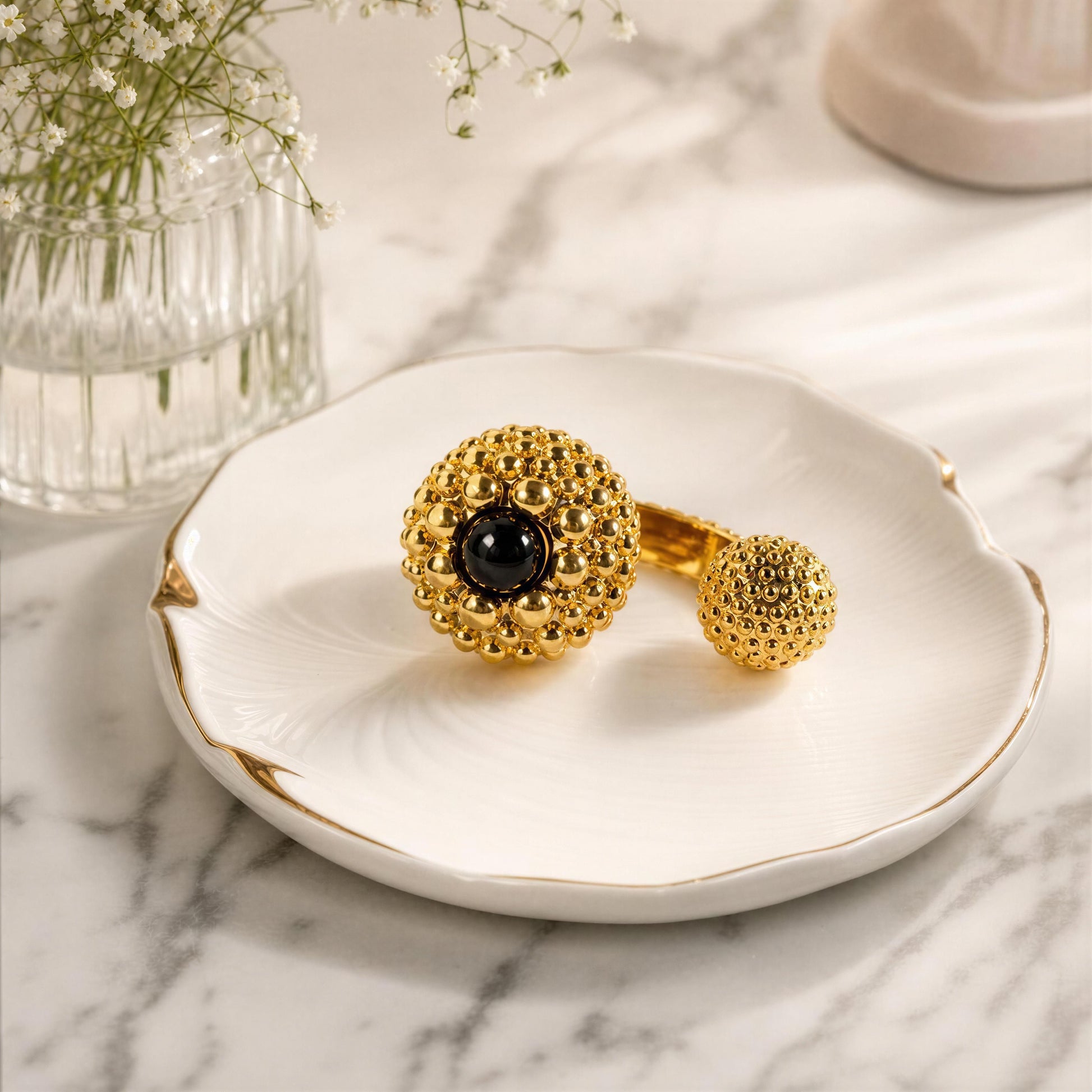The Nero Ring from Chica Chica Jewelry, displayed on a white scalloped dish with gold trim over a marble surface.