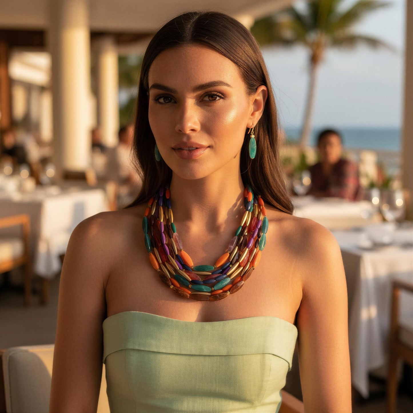 Woman wearing the Riviera Mosaic Necklace Set  in an outdoor setting with tables and people in the background