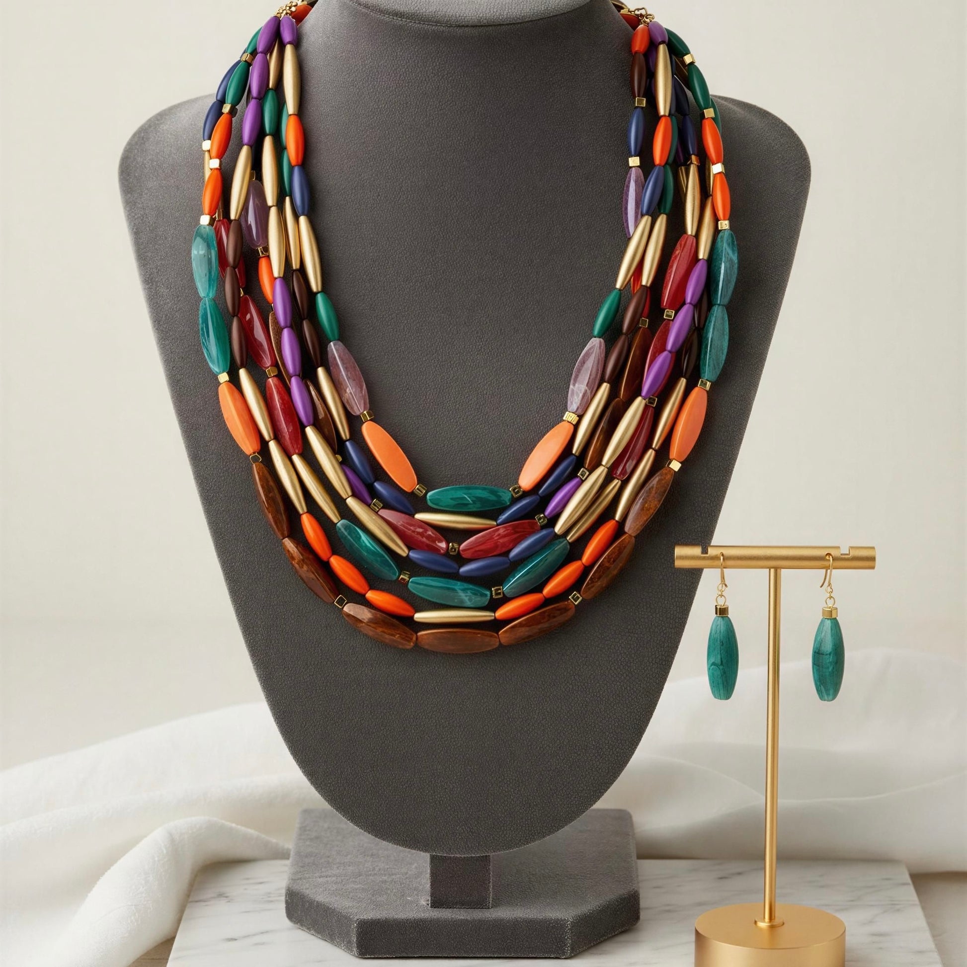 The Riviera Mosaic Necklace Set in a gray stand with a gold earring holder in the background.