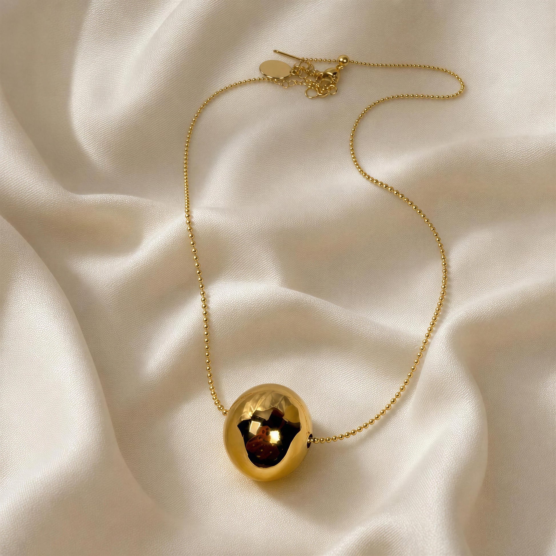 Gold necklace with a spherical pendant on a beige fabric background