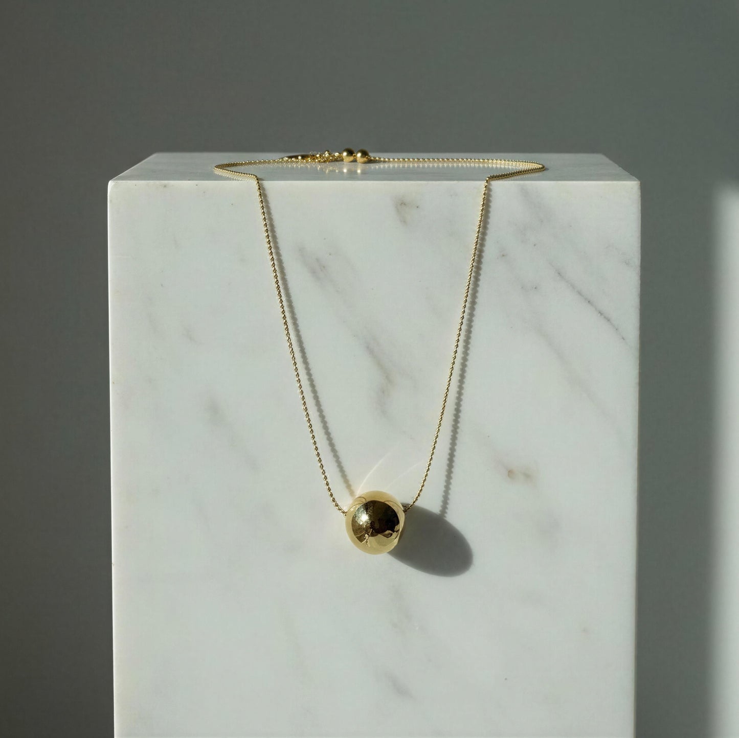 The Riviera Orb Necklace on a marble surface