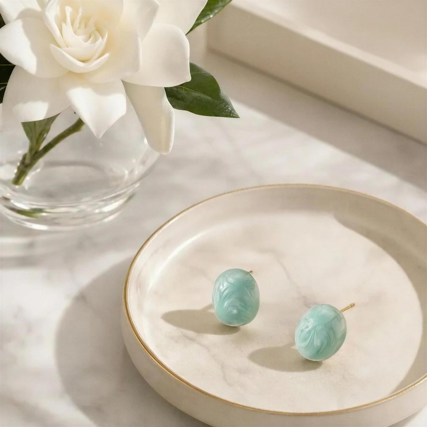 The Rosina Studs -Aqua Glow on a white dish with white flowers in the backgroundq