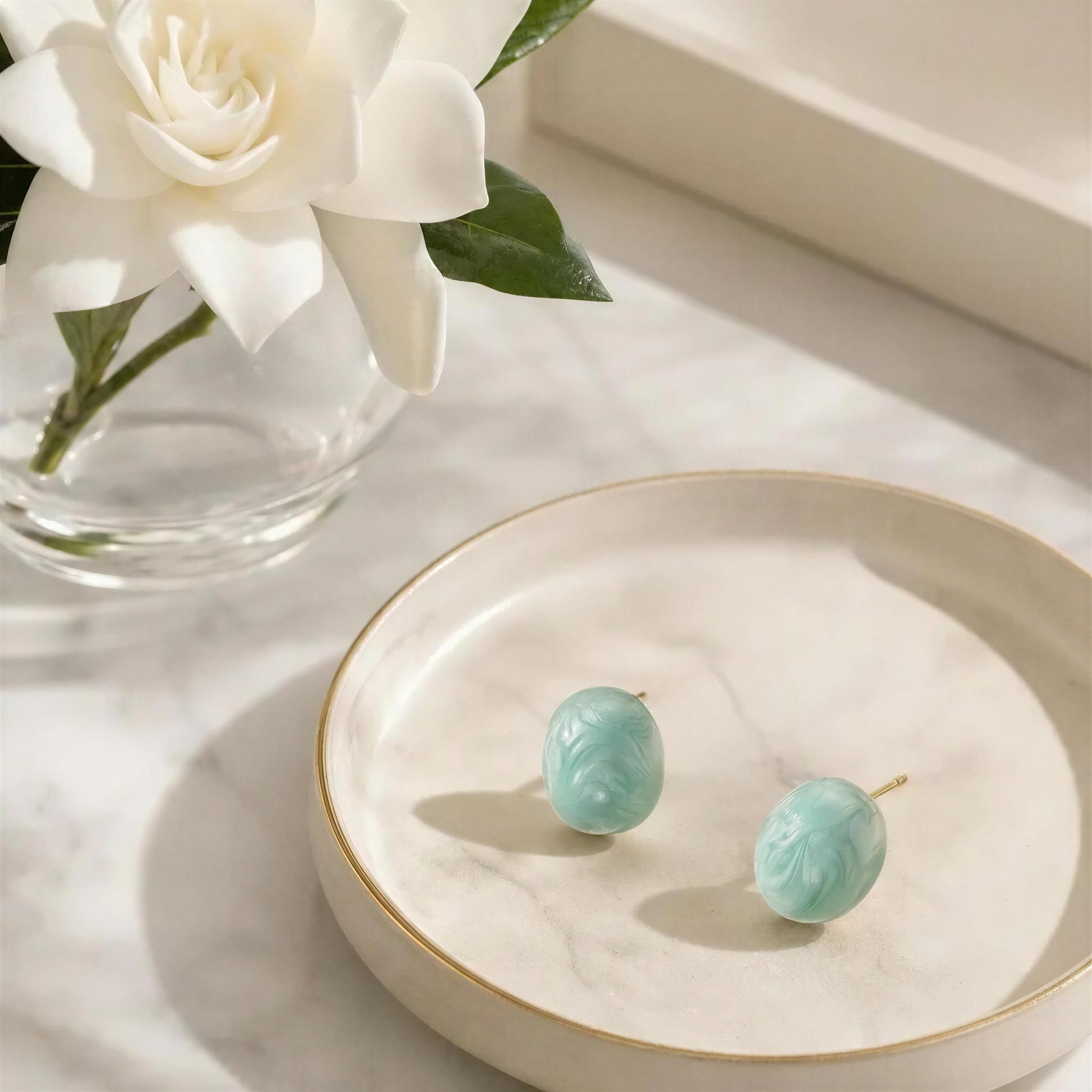 The Rosina Studs -Aqua Glow on a white dish with white flowers in the backgroundq