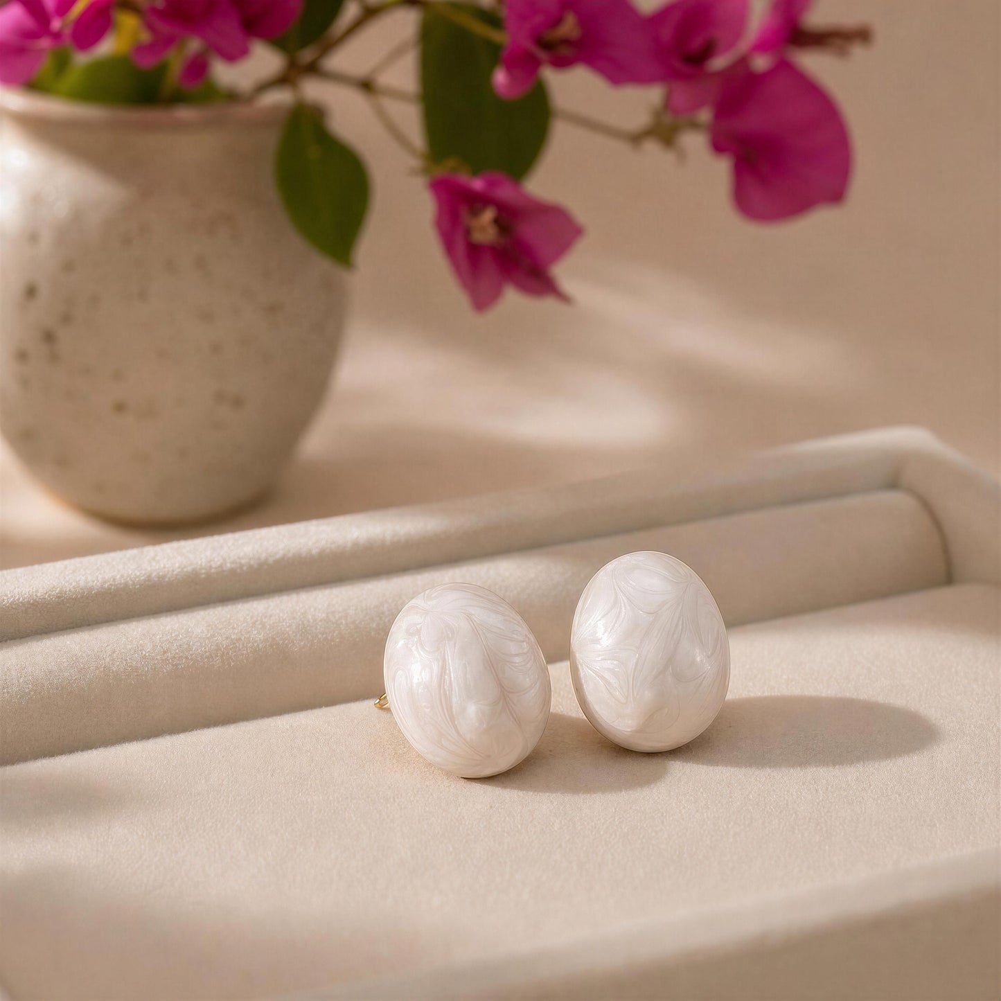 The Rosina Studs - Ivory Mist on a beige surface with a vase of pink flowers in the background