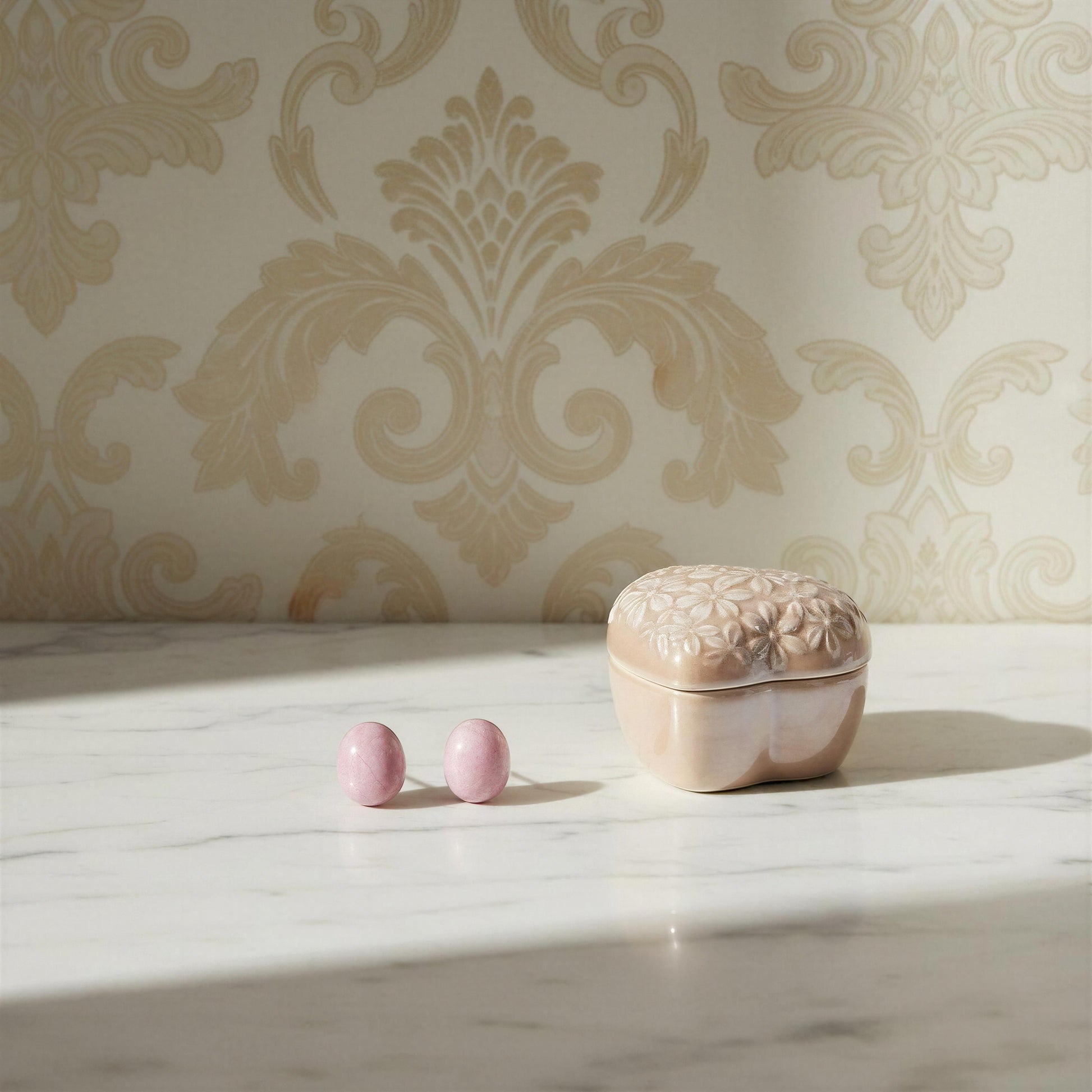 Pink earrings and decorative box on a marble surface with ornate wallpaper in the background
