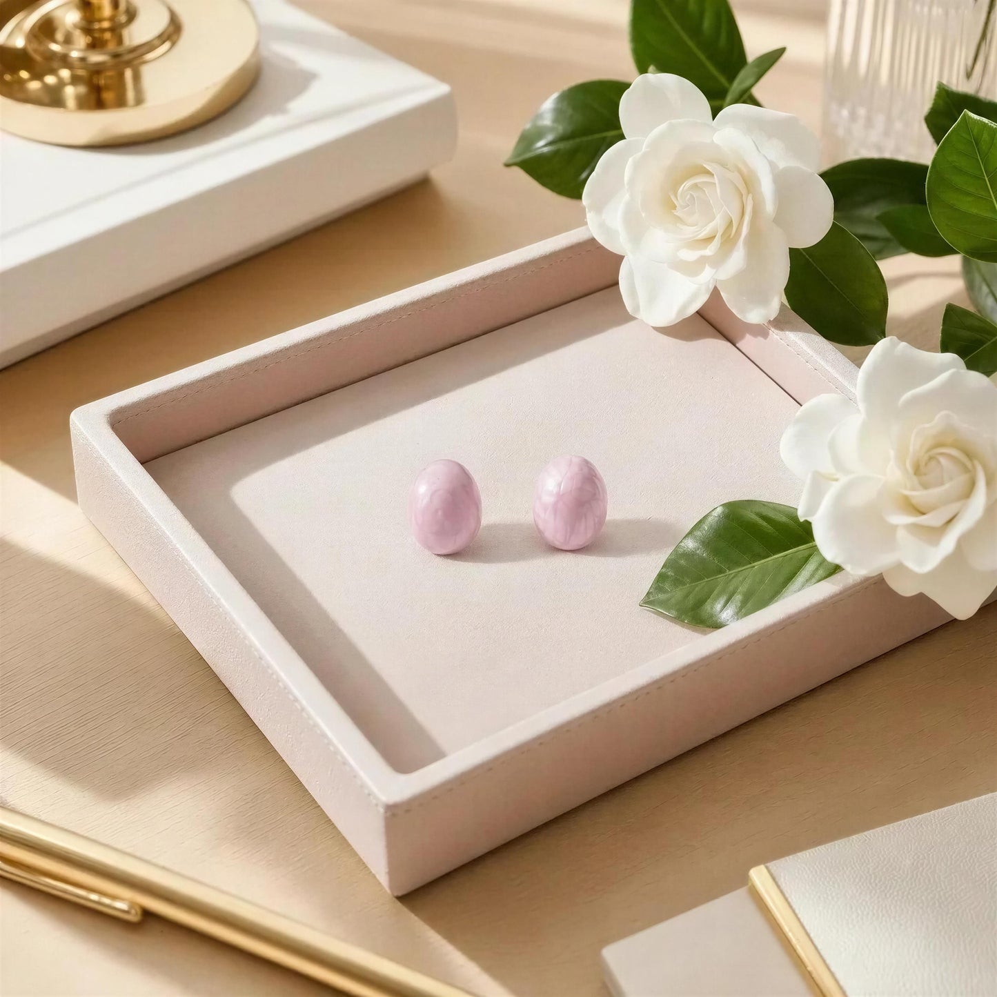 Pink earrings in a jewelry box with white flowers on a beige surface