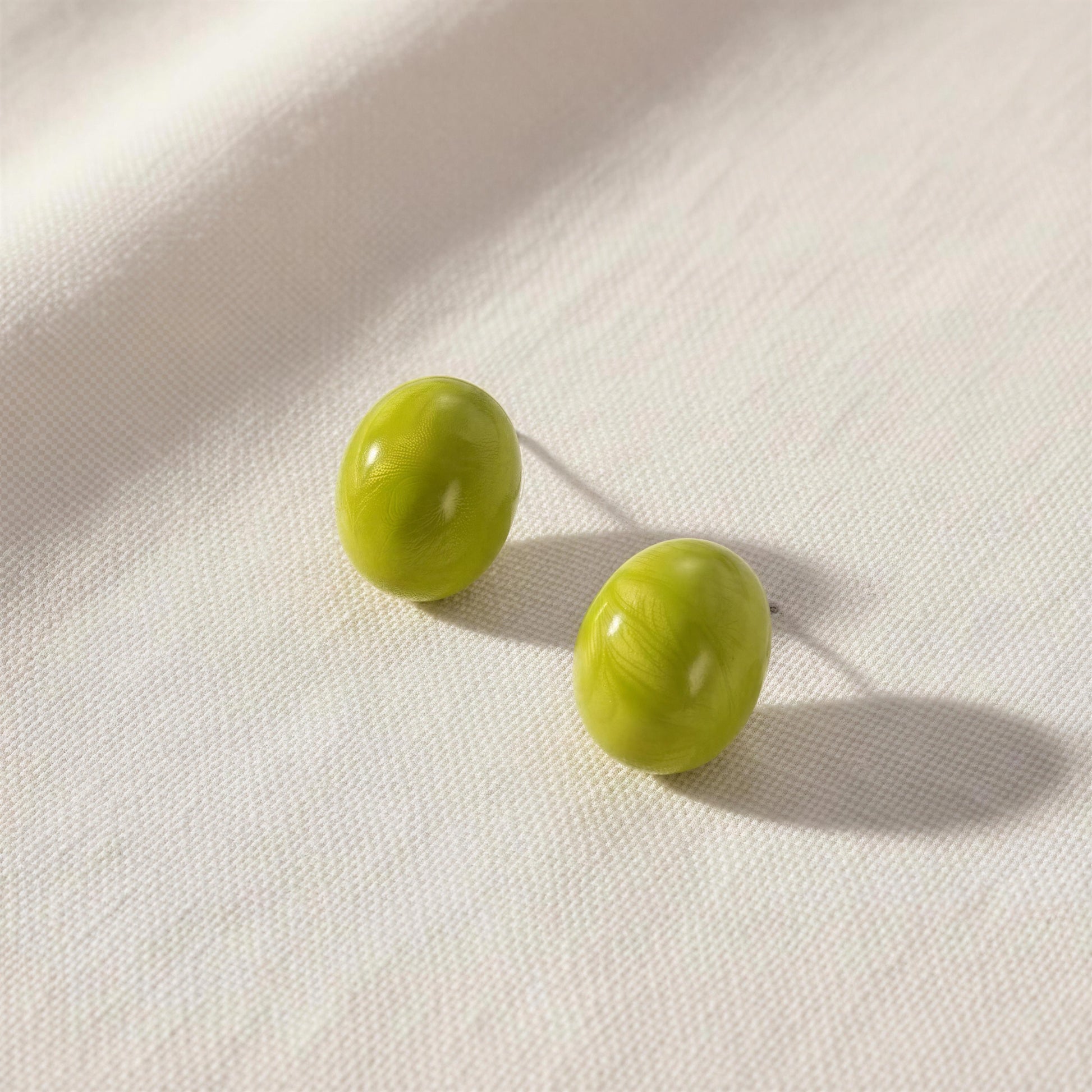 Two green stud earrings on a white fabric background