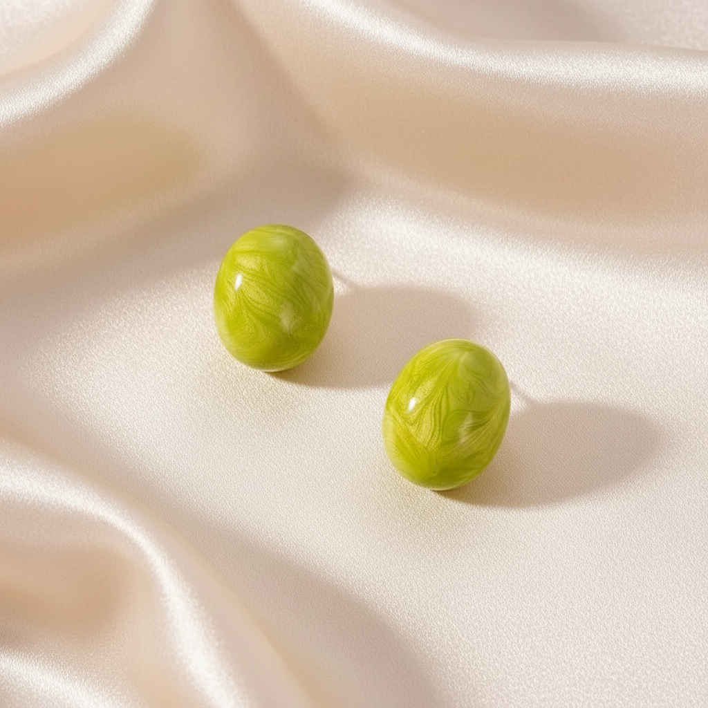 Rosina Studs in Verde Luxe displayed on soft ivory fabric, featuring glossy marbled green oval stud earrings.
