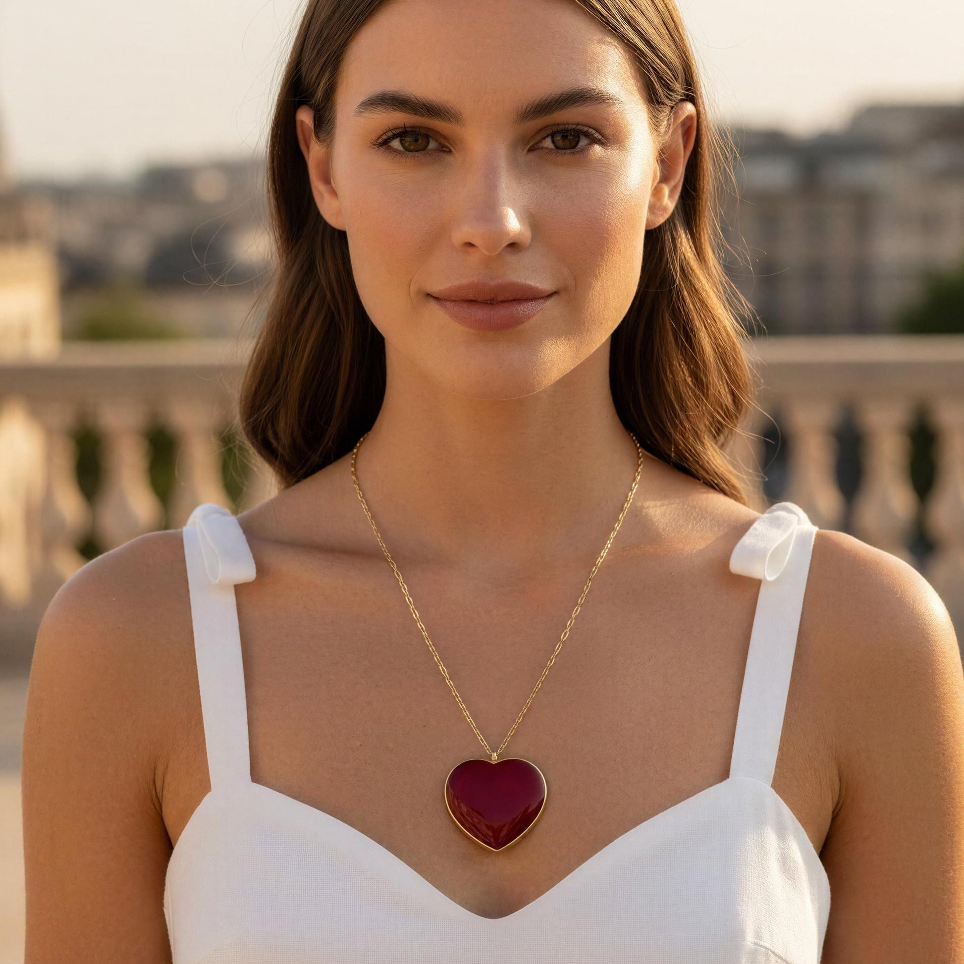 Woman wearing a white dress and gold necklace with a red heart pendant, standing outdoors.