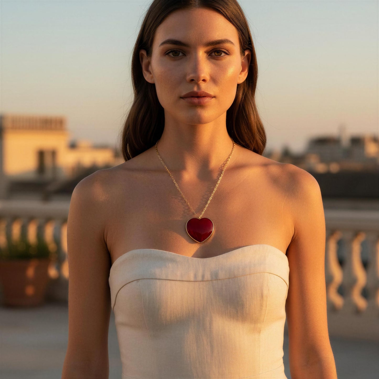 Woman wearing a strapless dress and Rosso Heart Necklace from Chica Chica Jewelry  with a heart pendant on a rooftop at sunset.