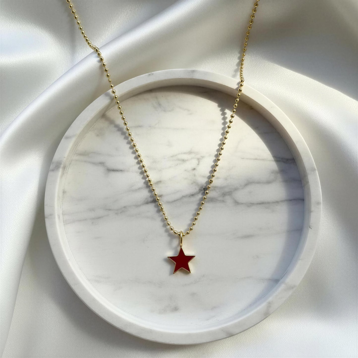 Gold necklace with a red star pendant on a marble surface