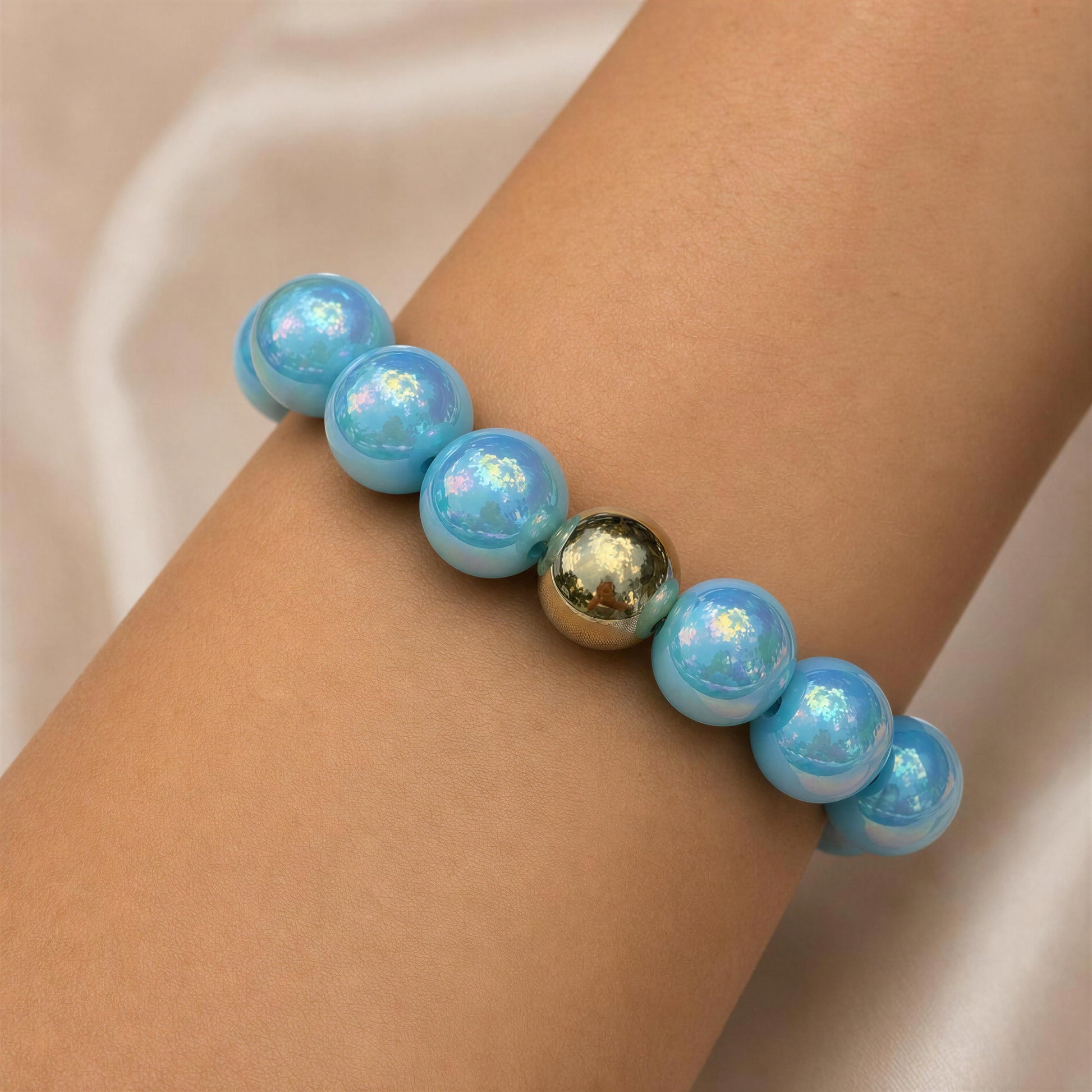 Bracelet with blue beads and a gold accent on a wrist against a beige background