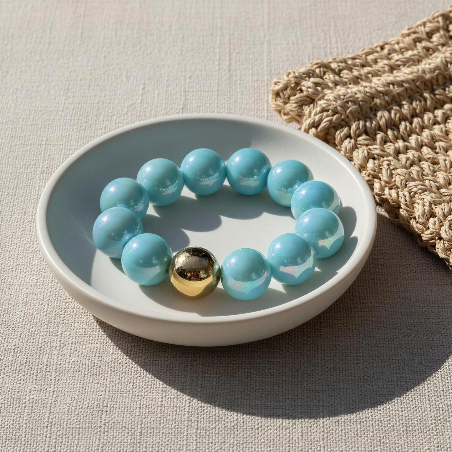 Turquoise beaded bracelet with a gold accent on a white dish, next to a woven basket.