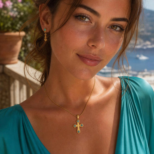A woman wearing the Serena turquoise cross necklace in 18K gold-plated stainless steel, set against a sunny outdoor coastal background.