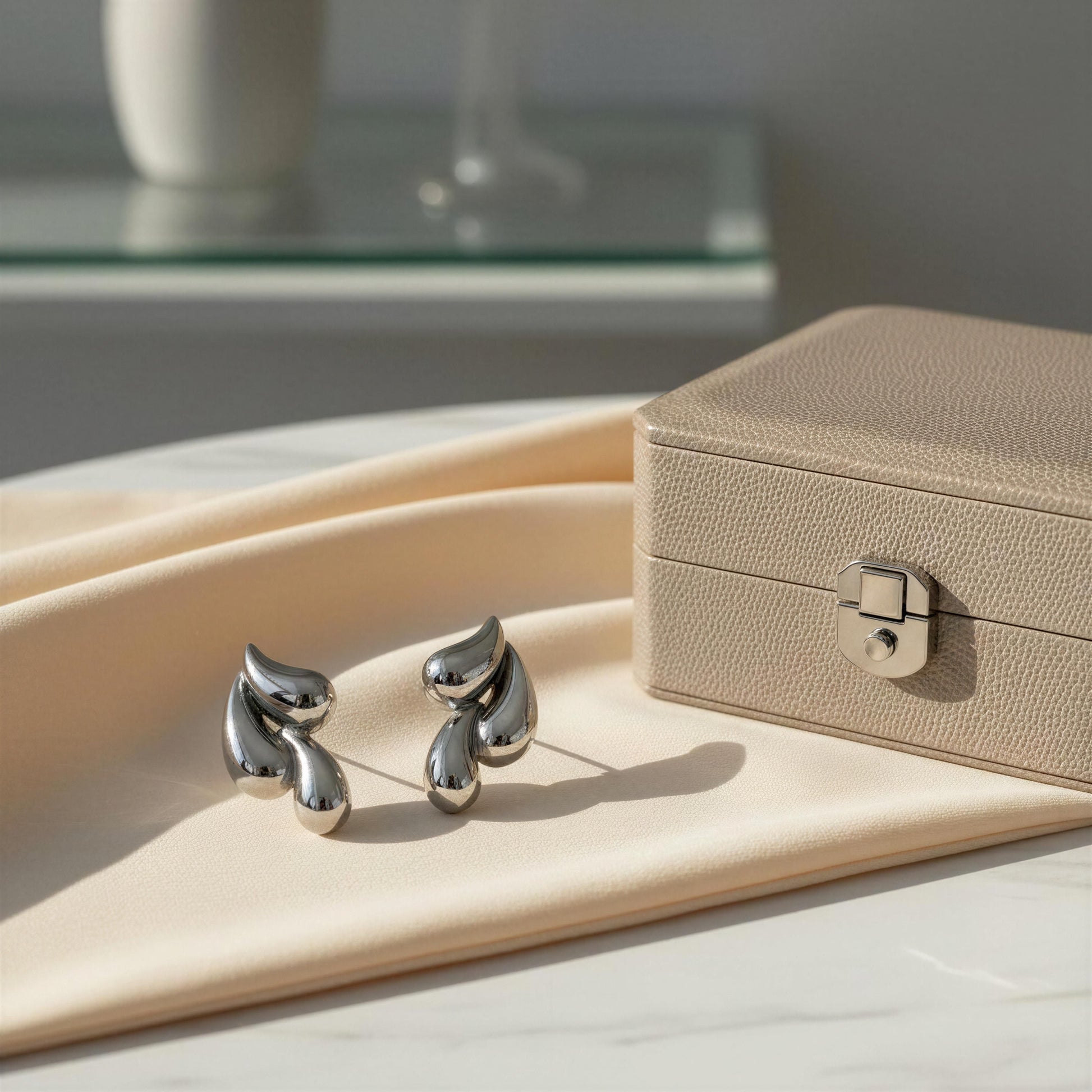 Silver earrings on a beige surface with a jewelry box in the background