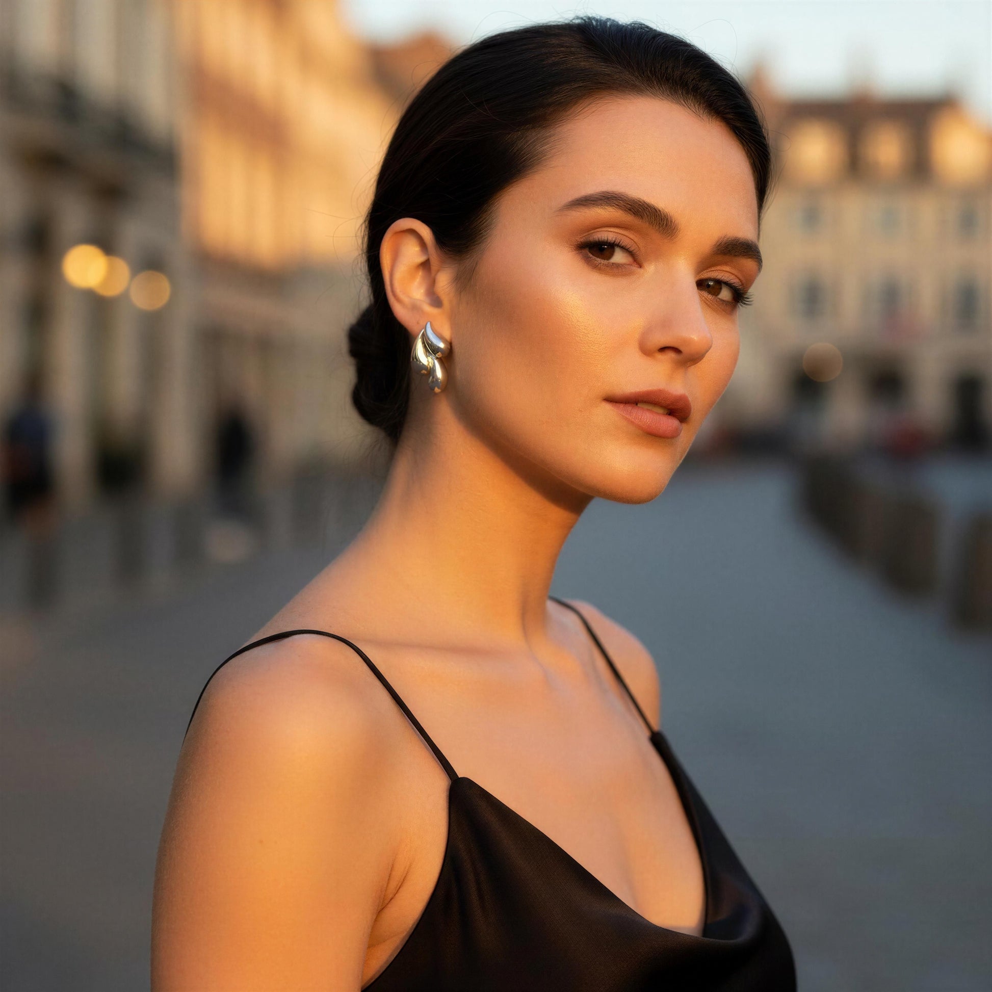 Woman in a black dress standing outdoors with a blurred background wearing the Silver Molten Wave Drop Earrings.