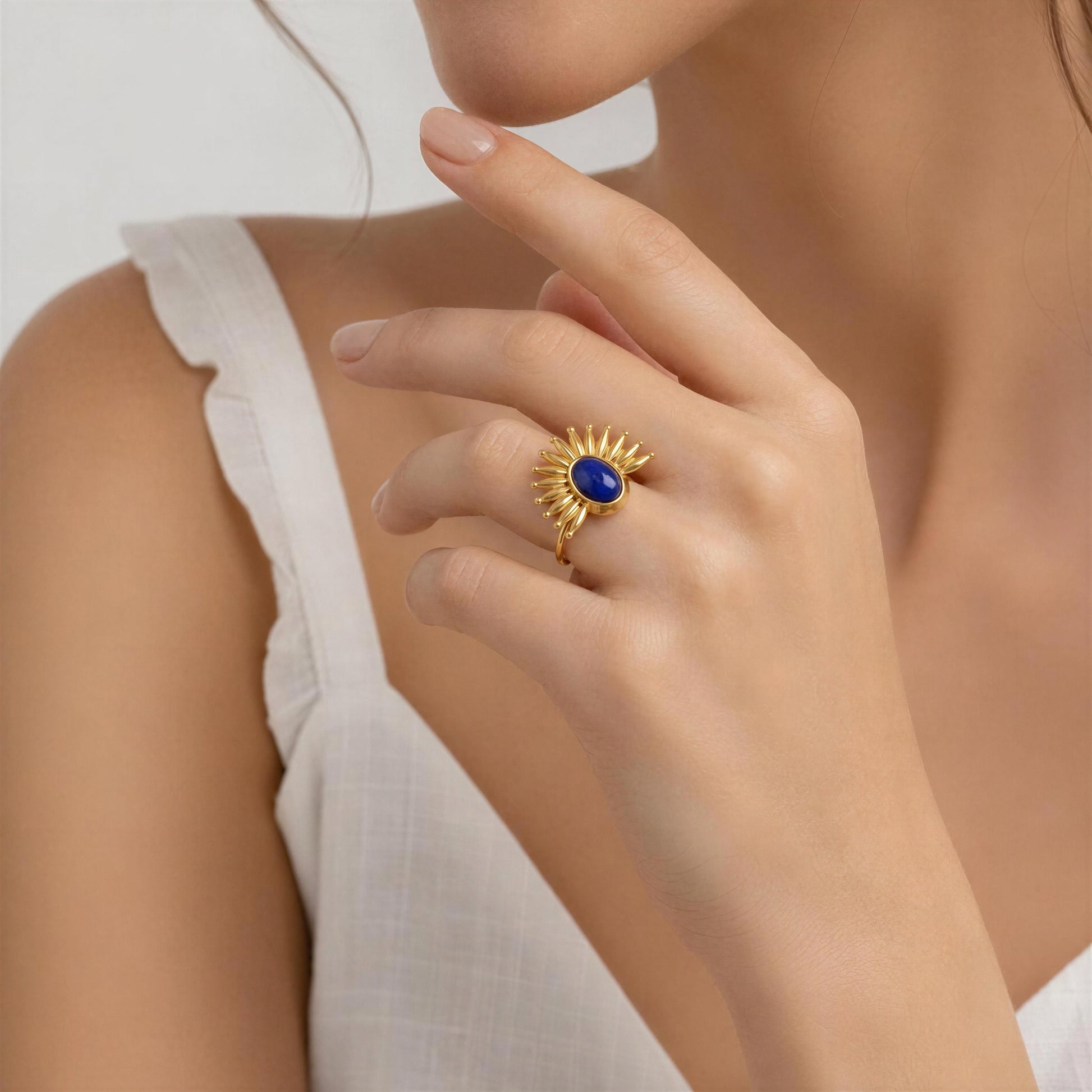 Gold ring with a blue gemstone on a person's finger against a neutral background