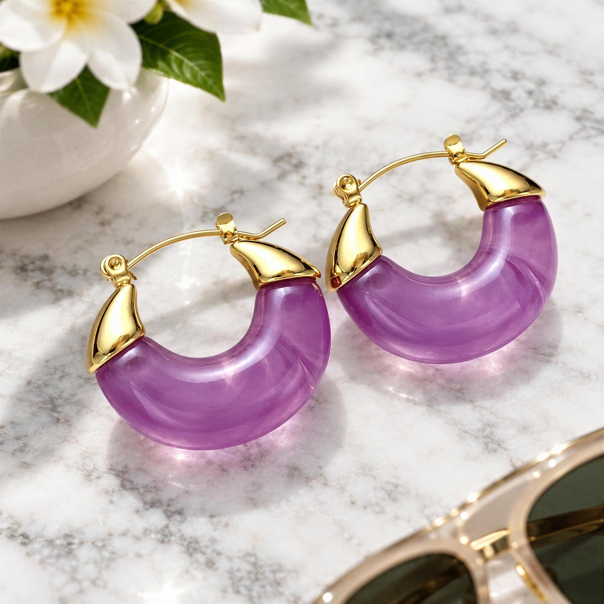 The Soraya Hoops – Violet from Chica Chica Jewelry on white marble table with tropical flowers and sunglasses. 