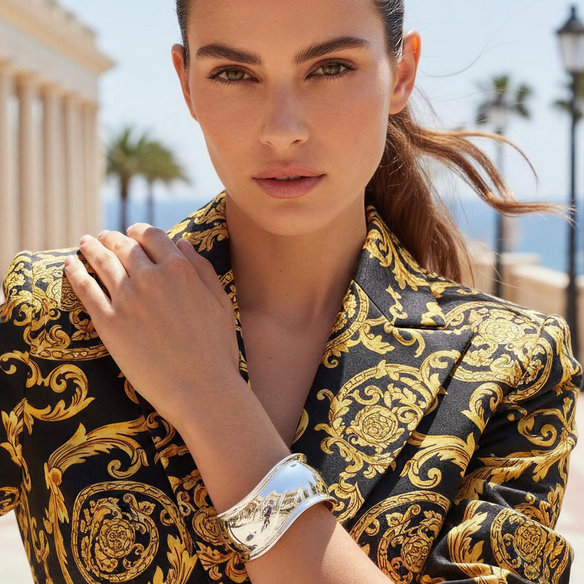 Model wearing the Forma Cuff in polished silver with a black and gold baroque-print blazer, showcasing its bold sculptural design and curved silhouette. Forma Cuff from Chica Chica Jewelry.