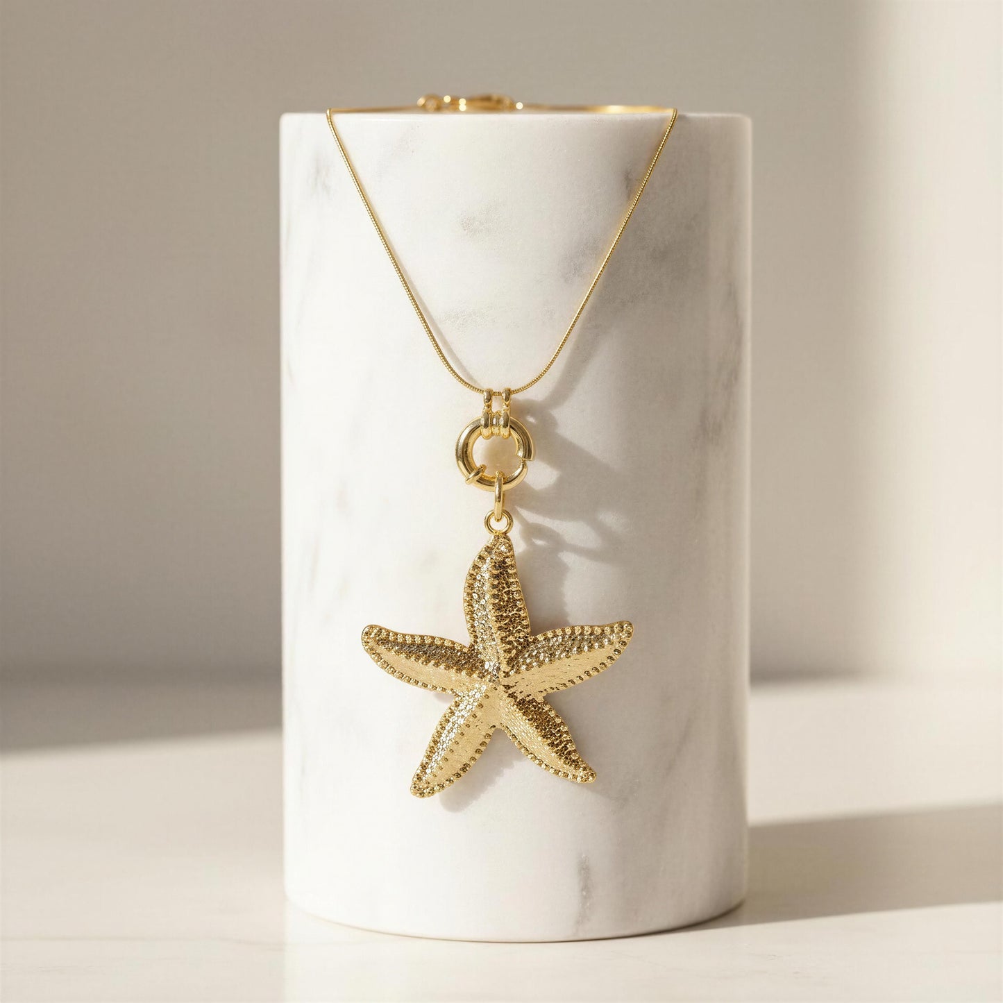 Gold starfish pendant necklace on a white cylindrical stand with a neutral background